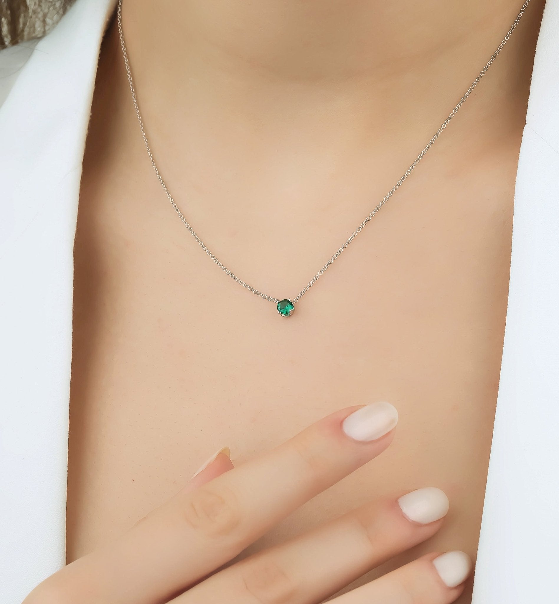 Close-up of a minimalist 14K white gold necklace featuring a 5mm prong set solitaire emerald, worn elegantly.