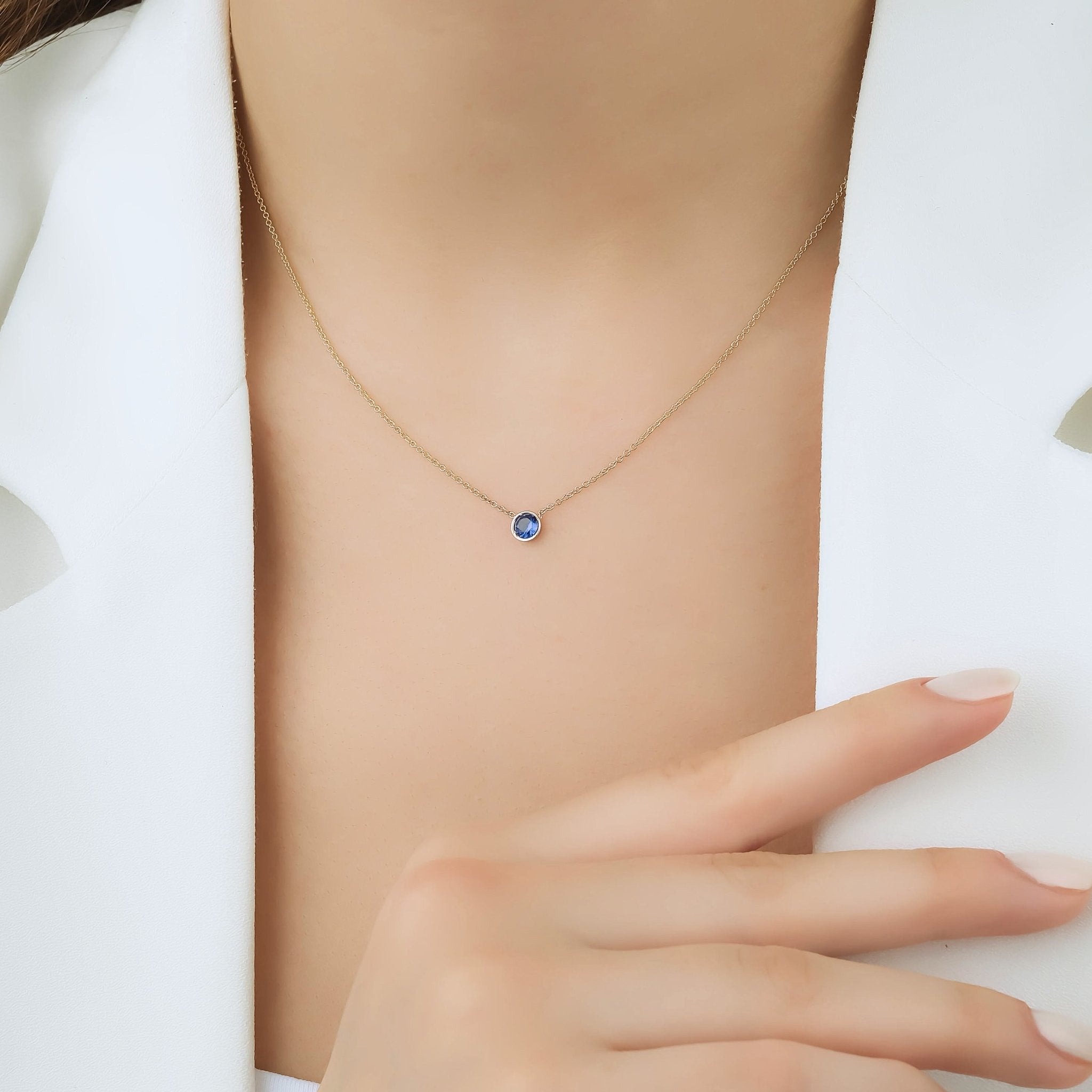Minimalist 14K white gold sapphire solitaire necklace worn on a model with a modern outfit.