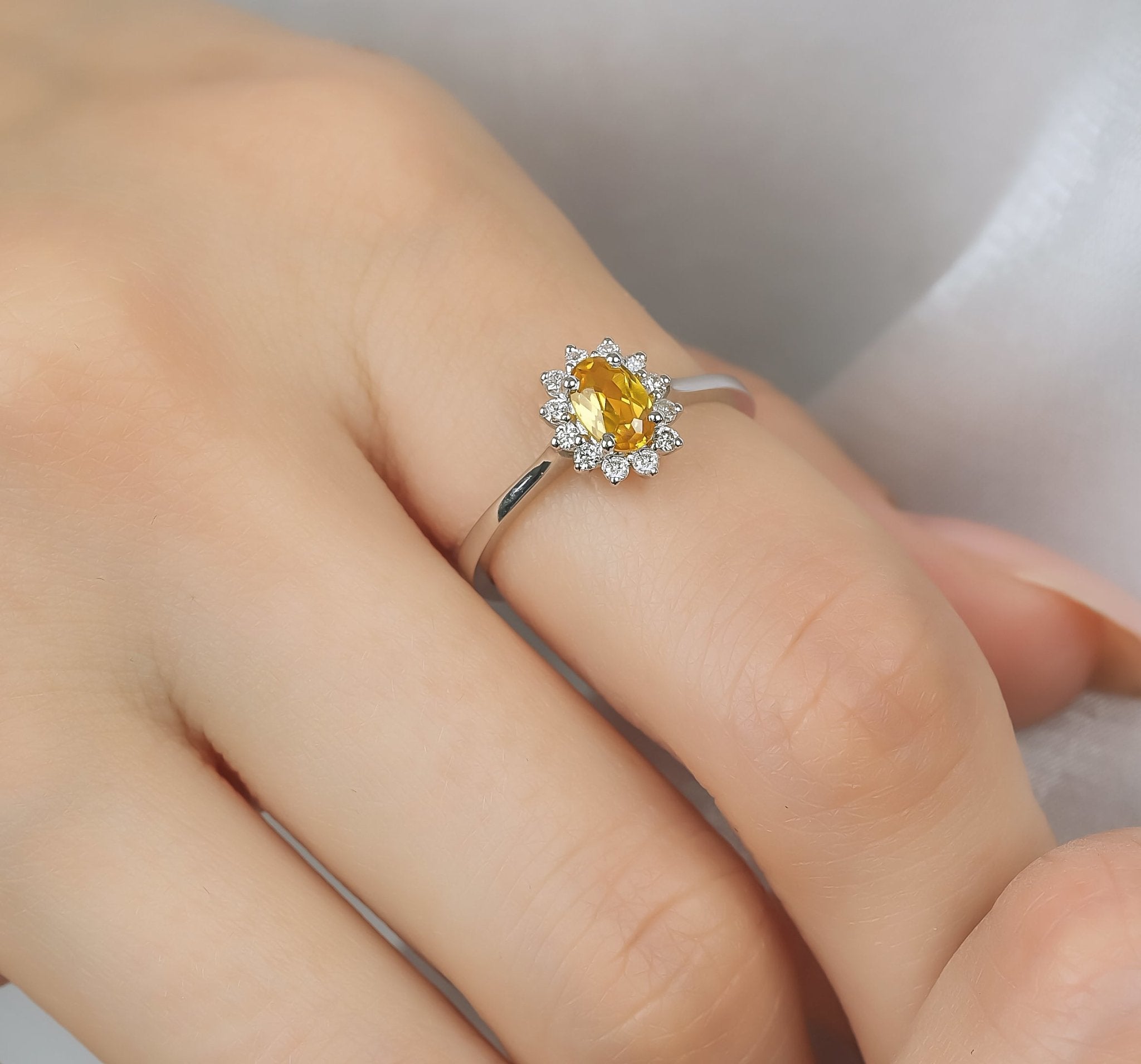 14K white gold oval citrine ring with diamond halo on finger, showcasing a 0.45 carat citrine gemstone and 12 round diamonds.