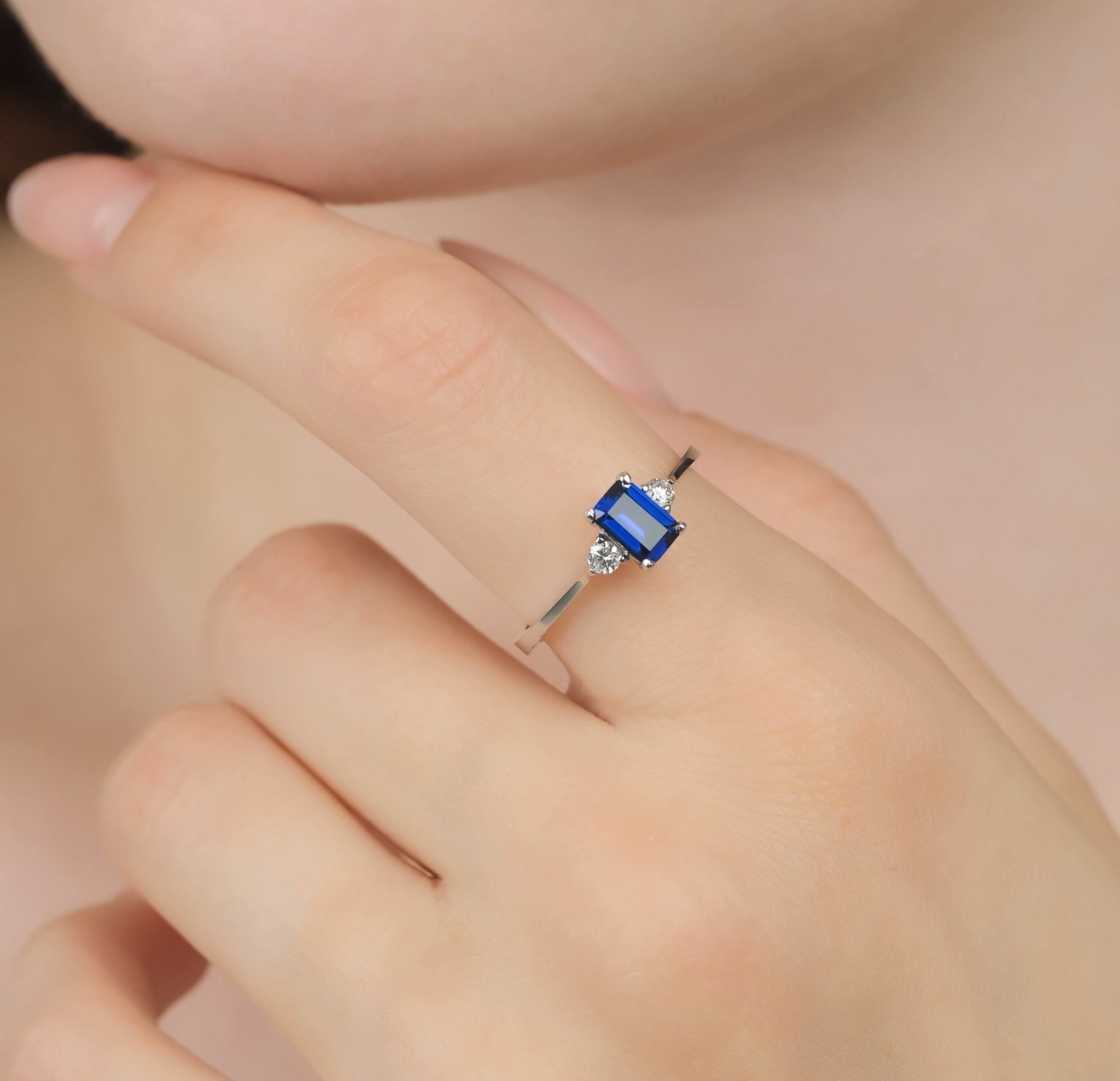 14K white gold emerald cut sapphire and diamond ring on a hand, featuring a blue sapphire and round diamonds.