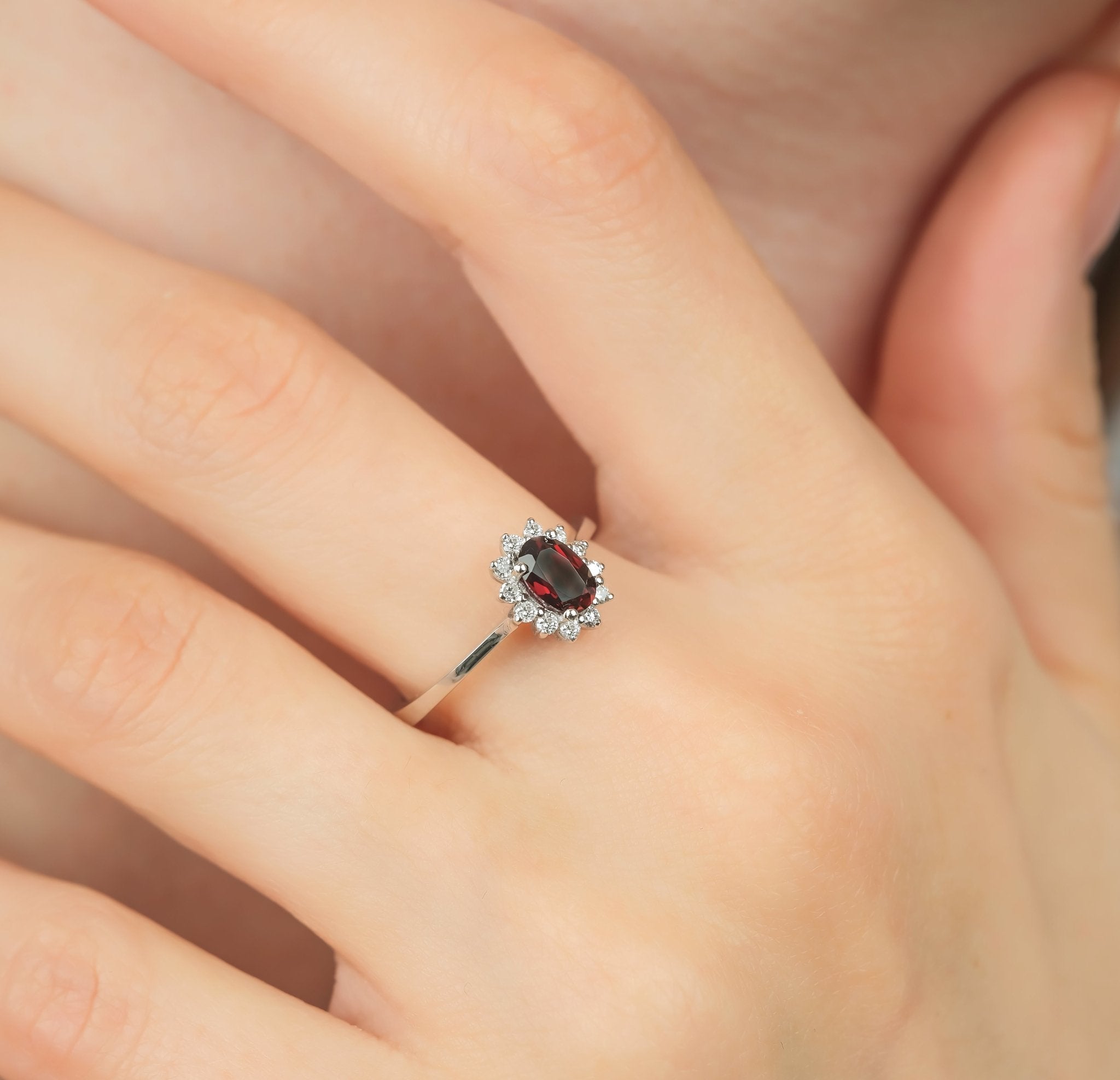 14K white gold women's oval garnet and diamond ring showcased on a hand, featuring 12 round diamonds and a 0.45 carat garnet.