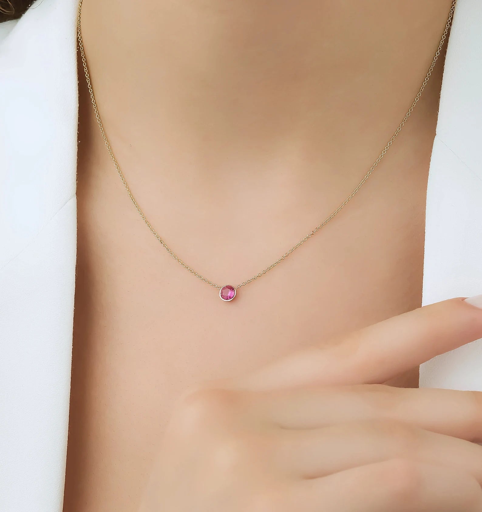 14K yellow gold minimalist necklace with 4mm bezel set ruby pendant, worn by a model in a close-up image.