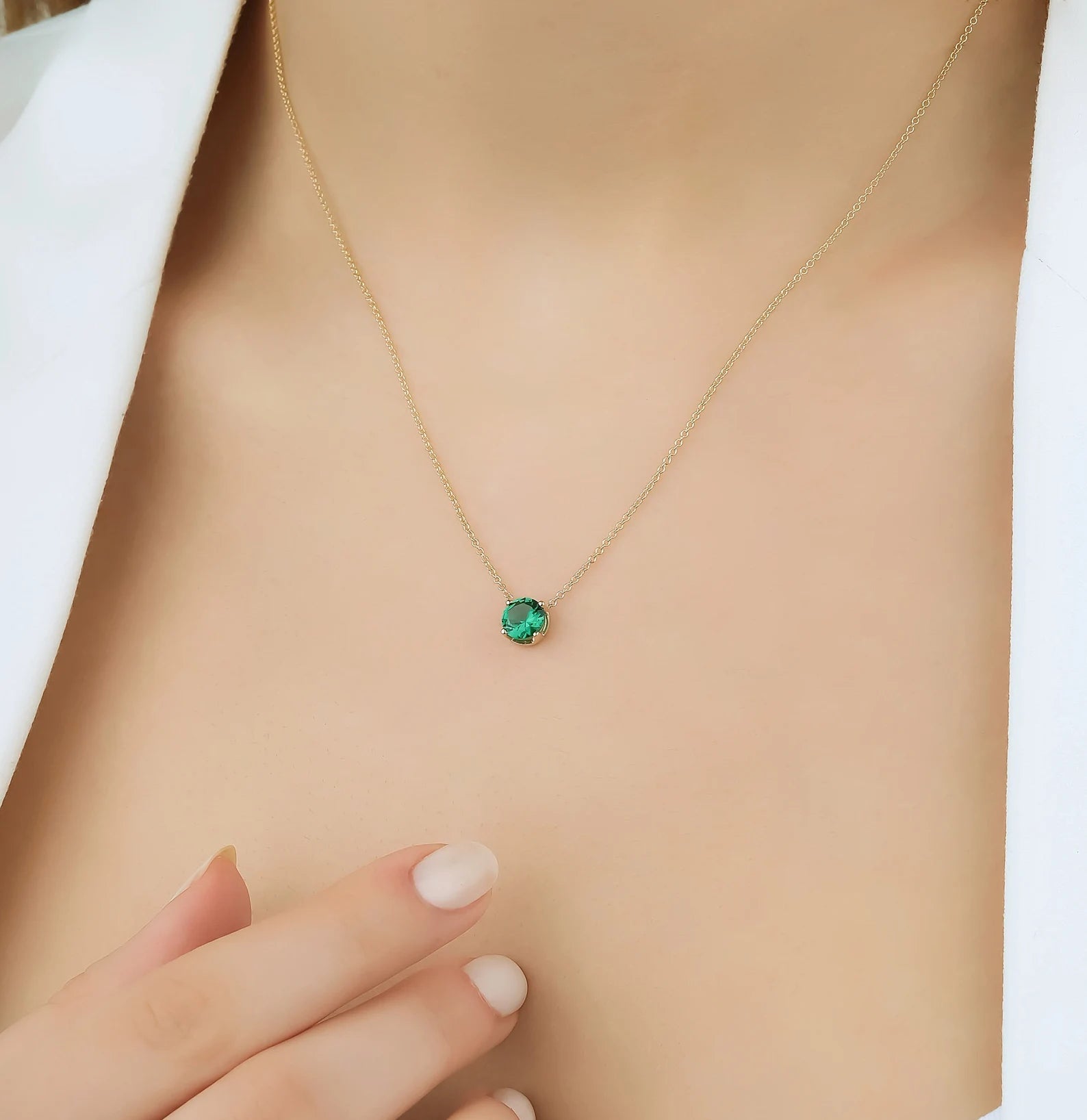 14K yellow gold 5mm prong setting minimalist emerald solitaire necklace on a model's neck.
