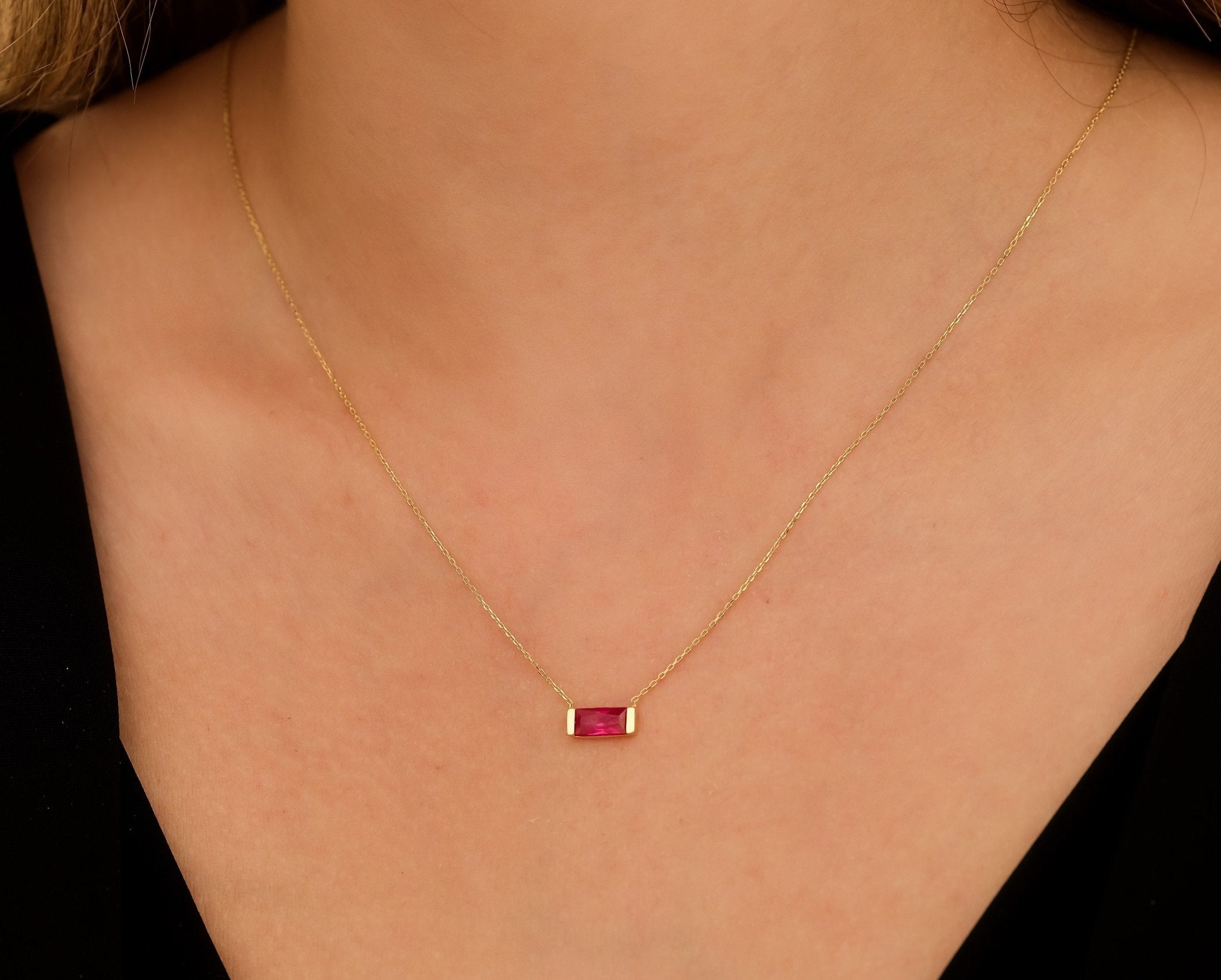 Dainty 14K yellow gold necklace featuring a minimalist baguette ruby pendant worn on a woman's neck.