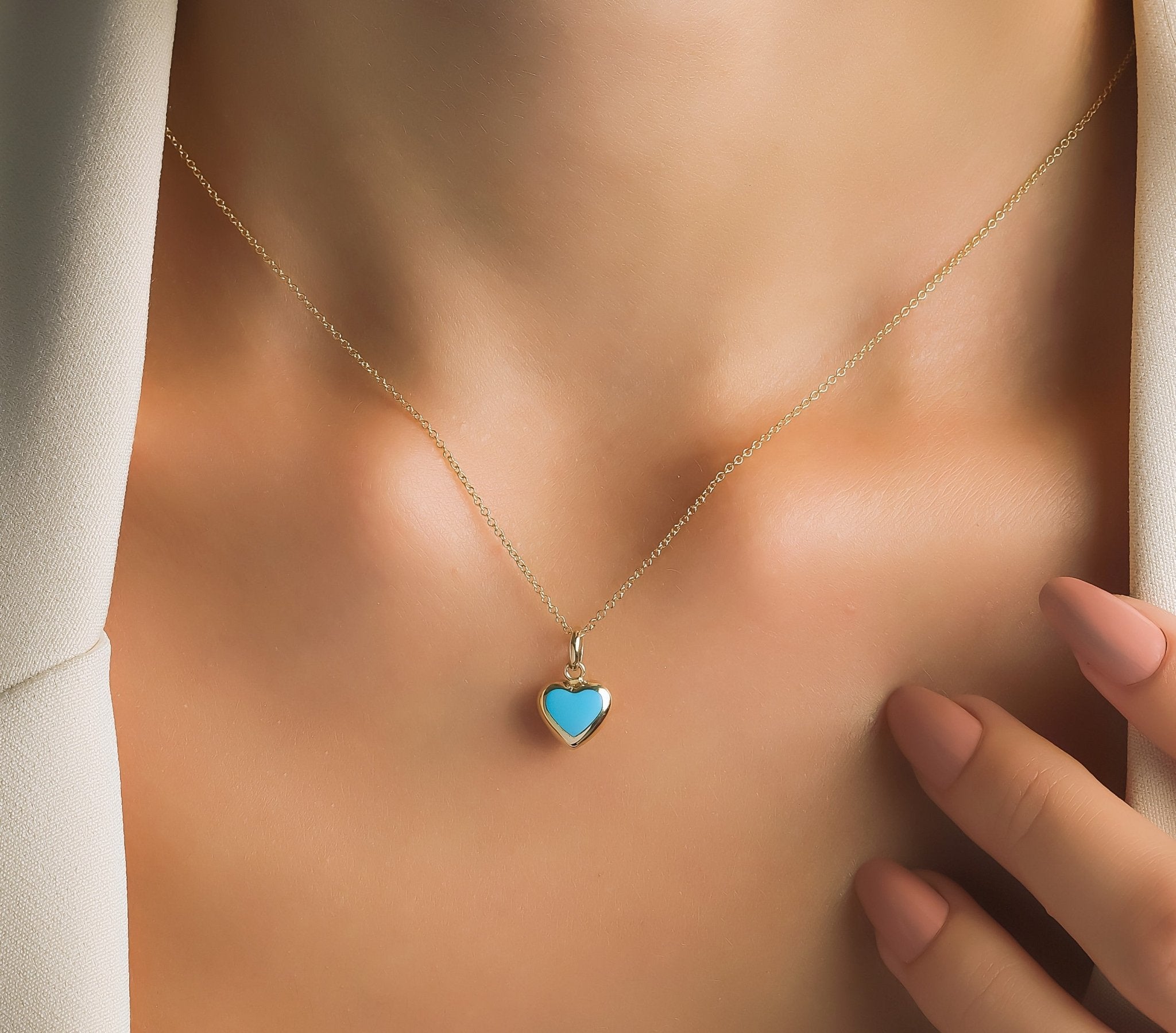 Lifestyle image of a woman wearing a 14K yellow gold minimalist turquoise puffed heart necklace, showcasing its dainty design.