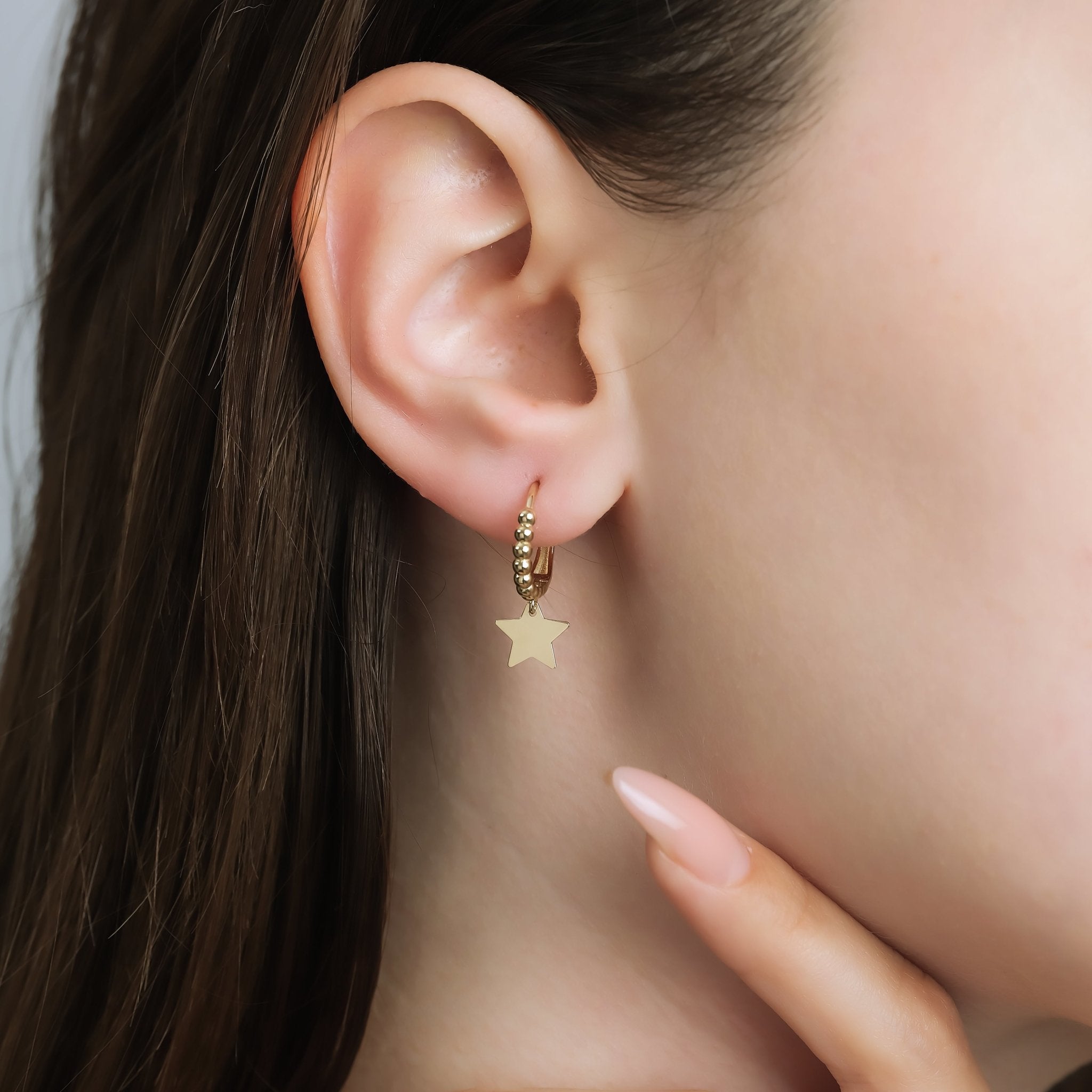 Model wearing 14K yellow gold dangle star hoop earrings, showcasing their elegance and design.