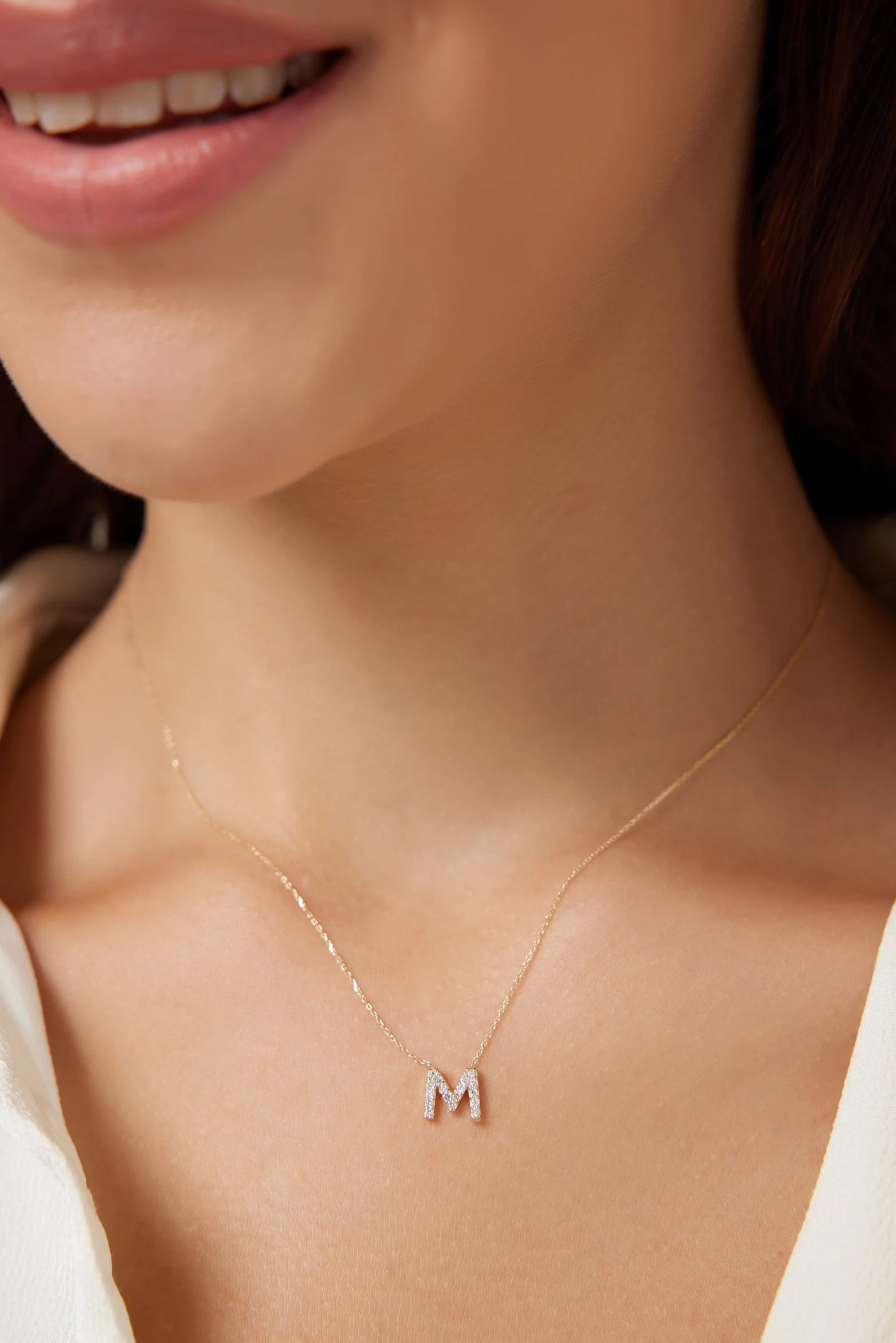 Woman wearing a 14K yellow gold diamond initial necklace featuring the letter M, showcasing its dainty design and sparkle.