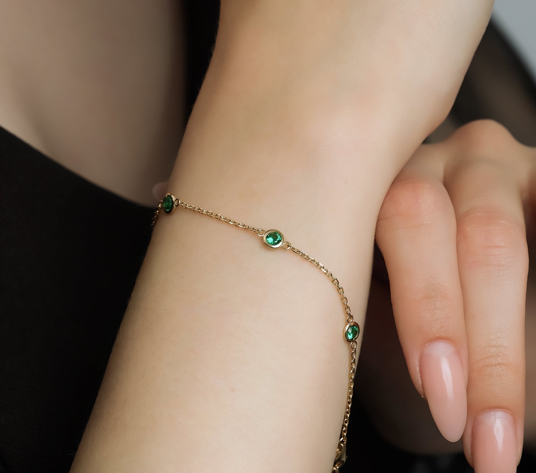 14K yellow gold bracelet featuring emeralds on a model's wrist, showcasing its delicate design and elegant style.