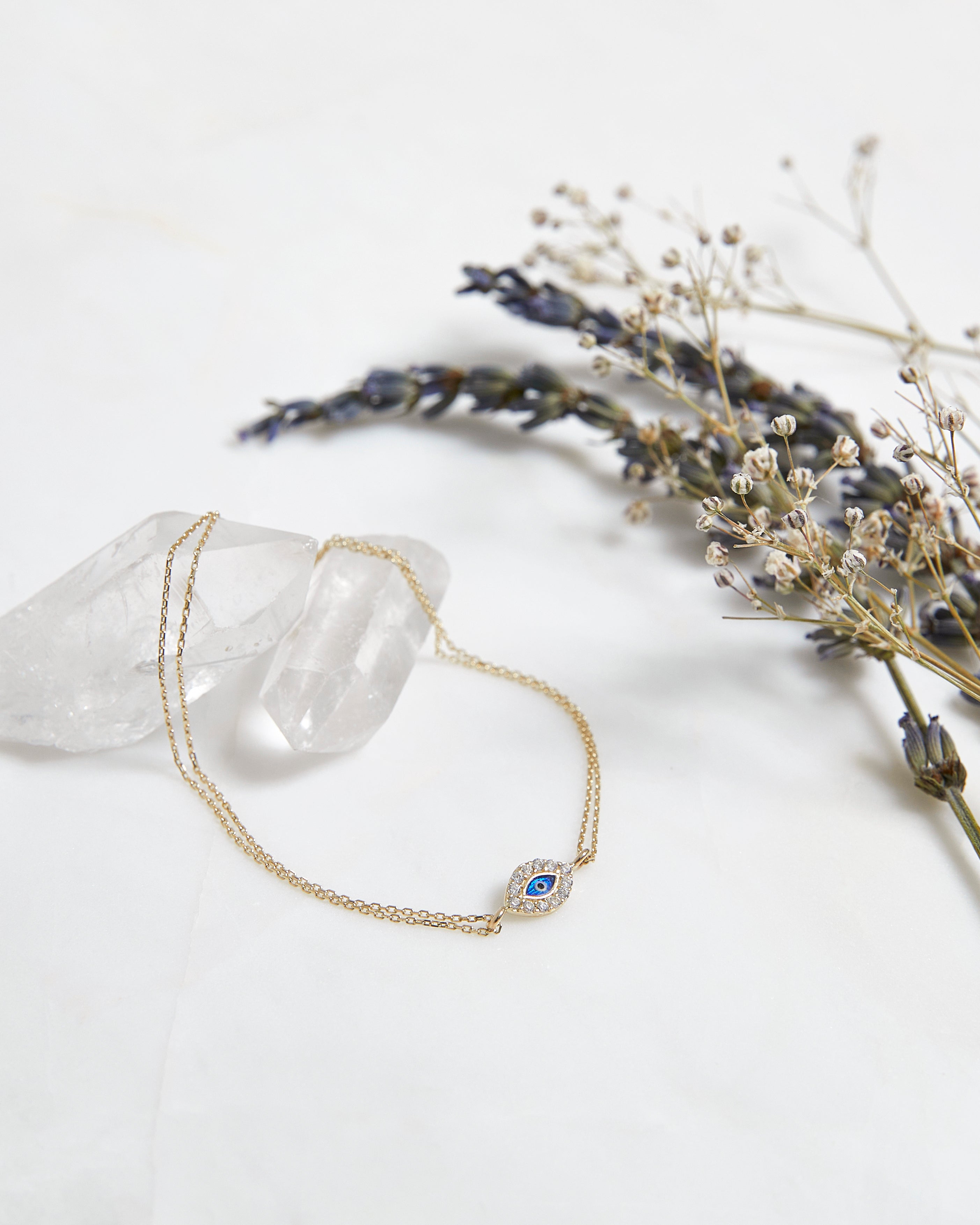 14K yellow gold minimalist evil eye bracelet with CZ on a neutral background with dried flowers.