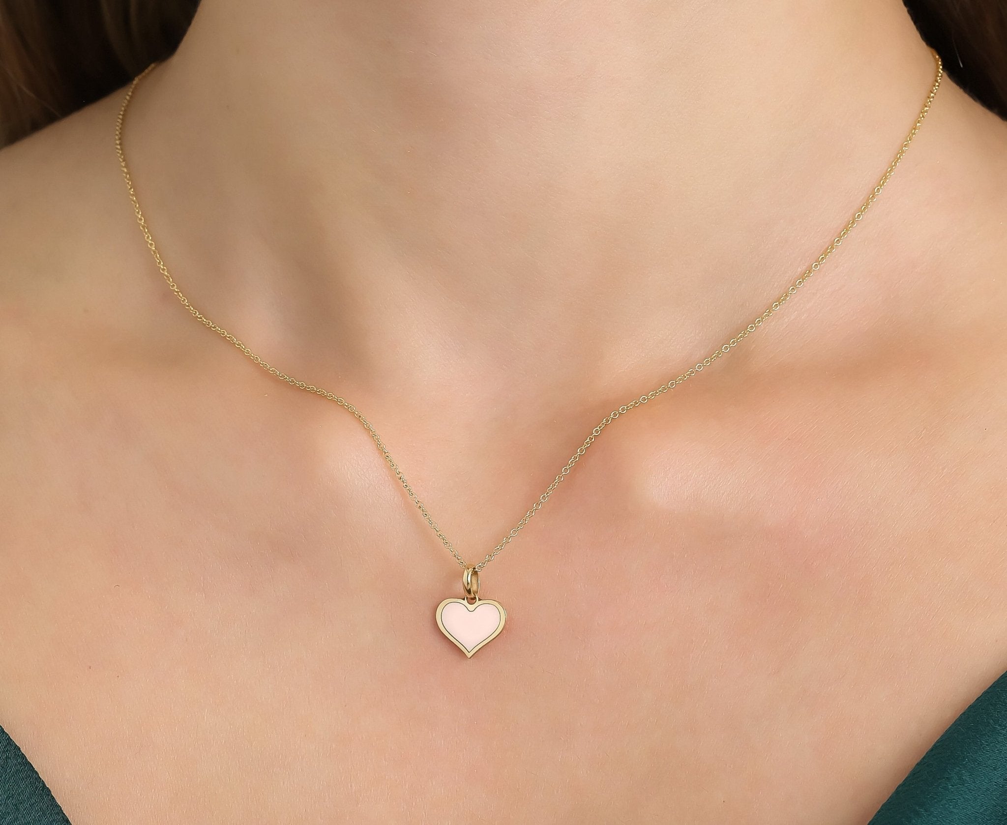 Dainty 14K yellow gold flat pink heart necklace worn on a model's neck, showcasing its elegant design and simplicity.