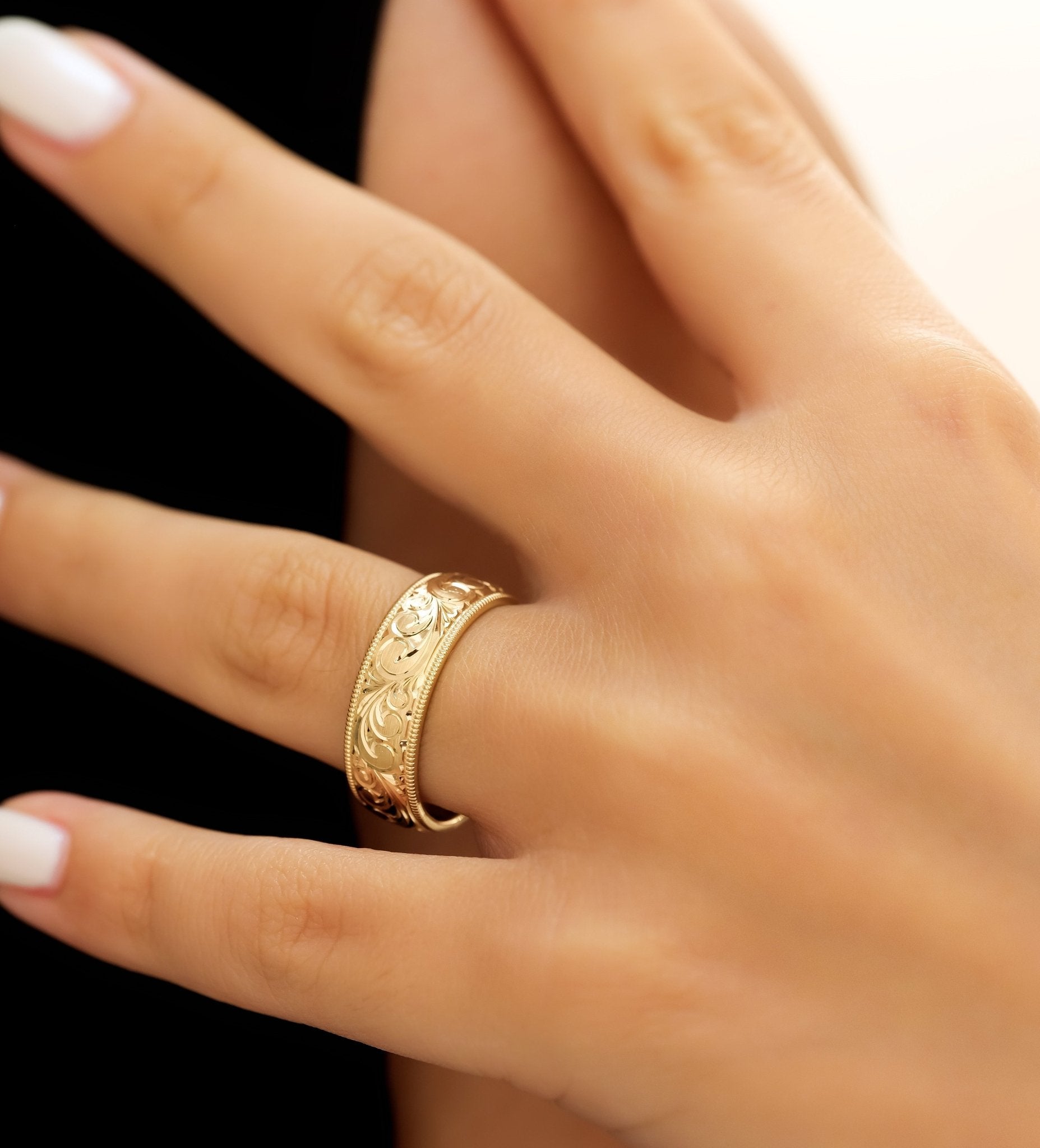 14K yellow gold hand engraved men's wedding band displayed on a hand with a shiny finish and leaf motif.