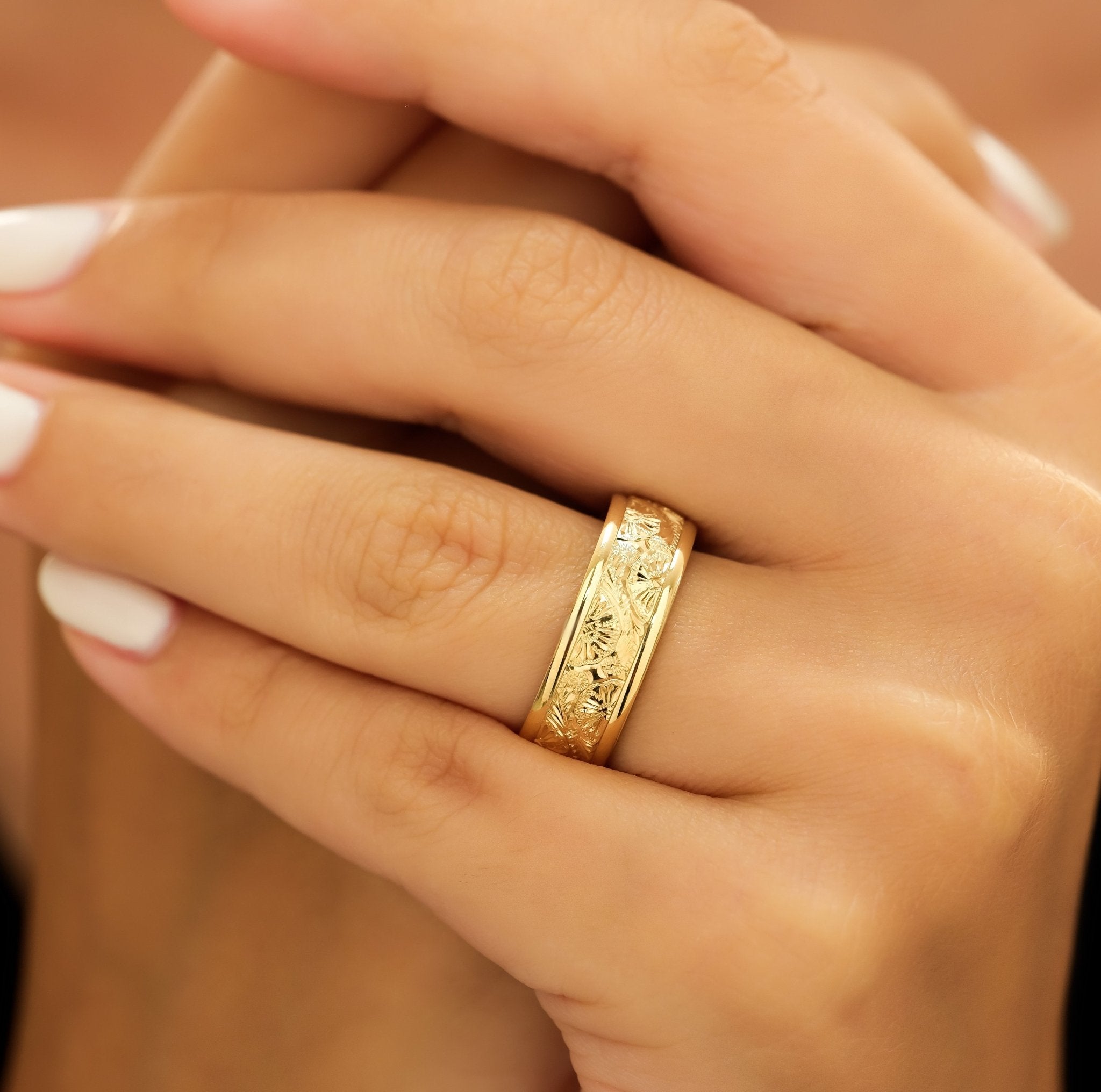 14K yellow gold hand engraved men's wedding band with shiny finish and leaf motif seen on a hand.