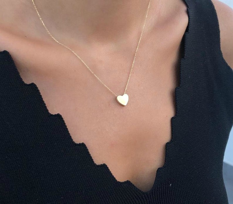 14K yellow gold minimalist heart necklace worn against a black top, showcasing a delicate and classy design.