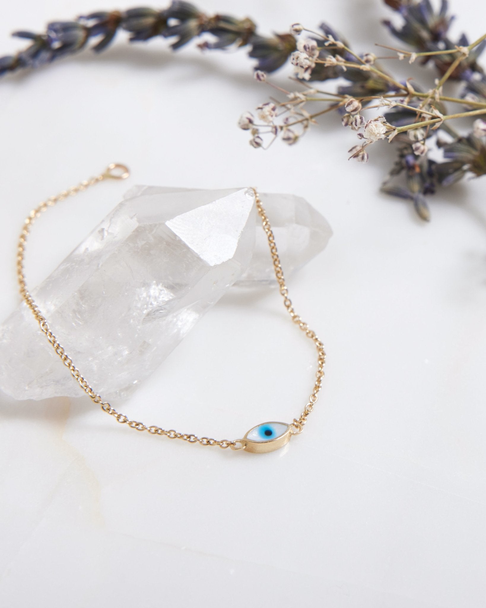 14K yellow gold minimalist eye shape evil eye bracelet with white enamel, set on a crystal background.