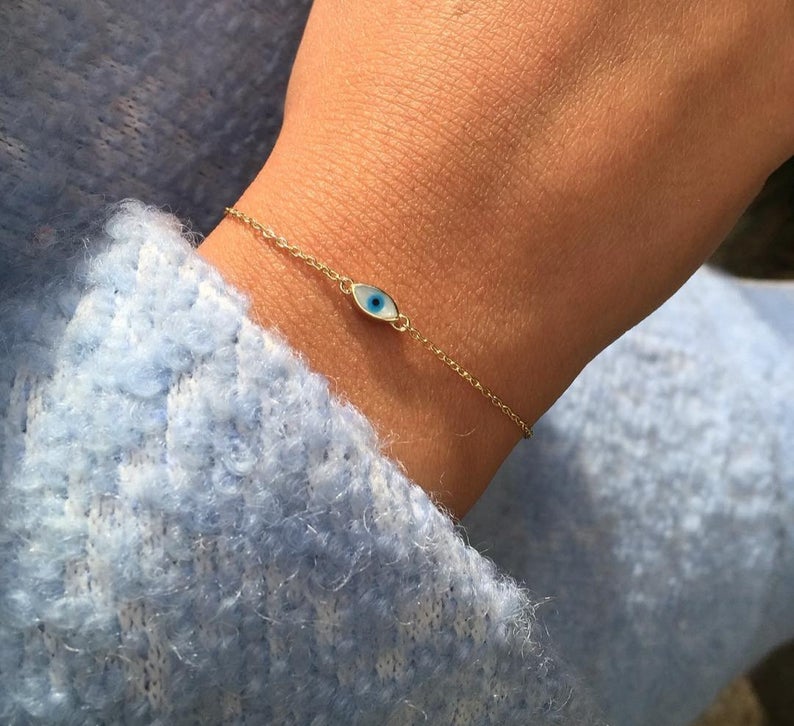 Woman wearing a 14K yellow gold minimalist evil eye bracelet with blue enamel detail.