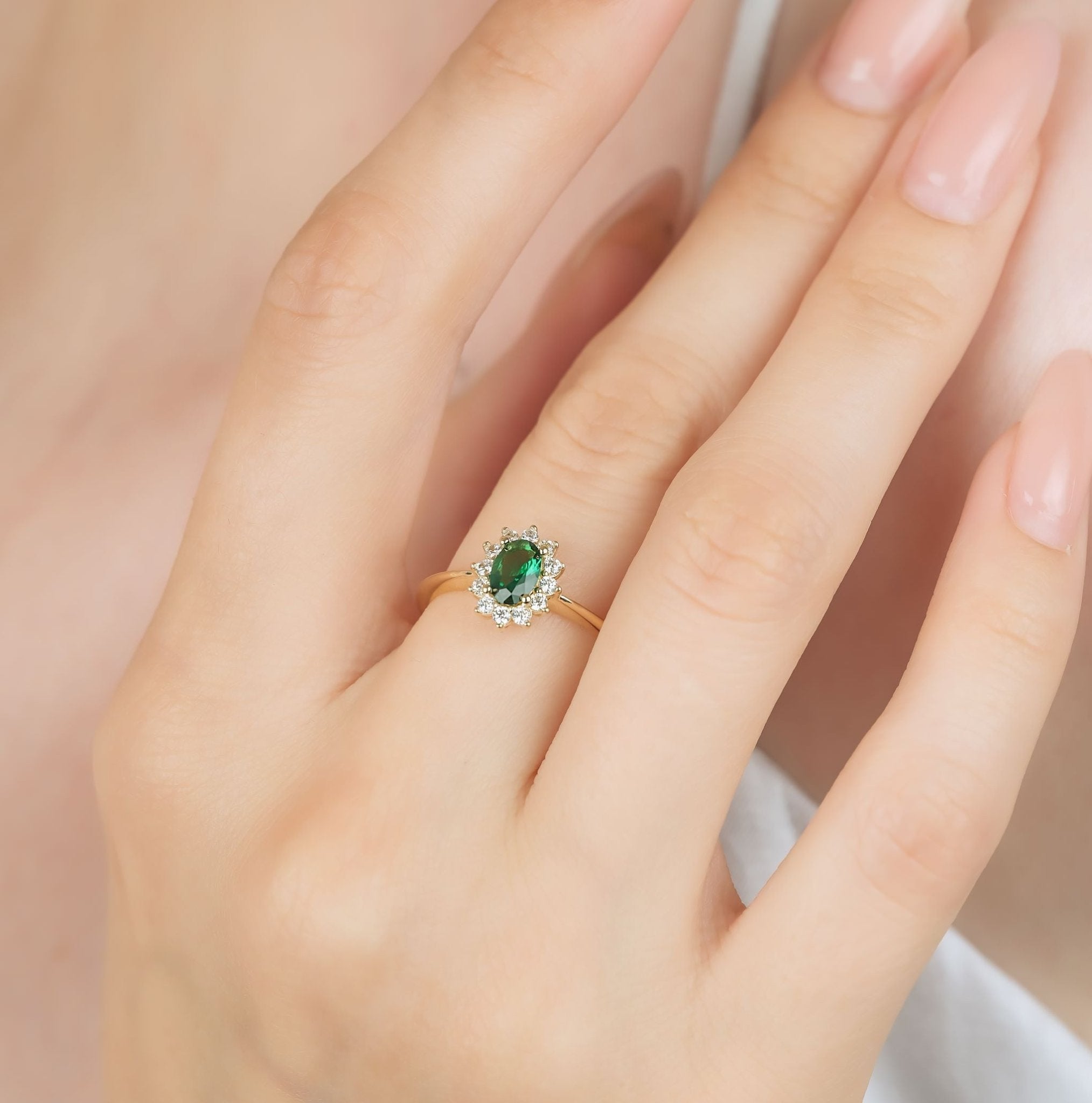 14K yellow gold oval emerald ring on a woman's finger, featuring CZ side stones, showcased in elegant style.