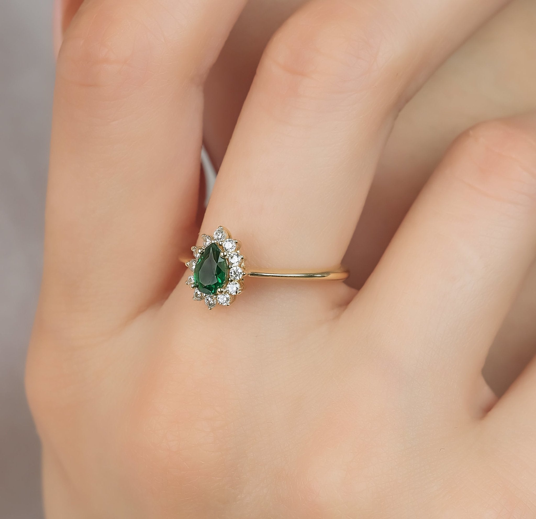 Elegant 14K yellow gold ring featuring a pear shape emerald center stone surrounded by sparkling cubic zirconia.