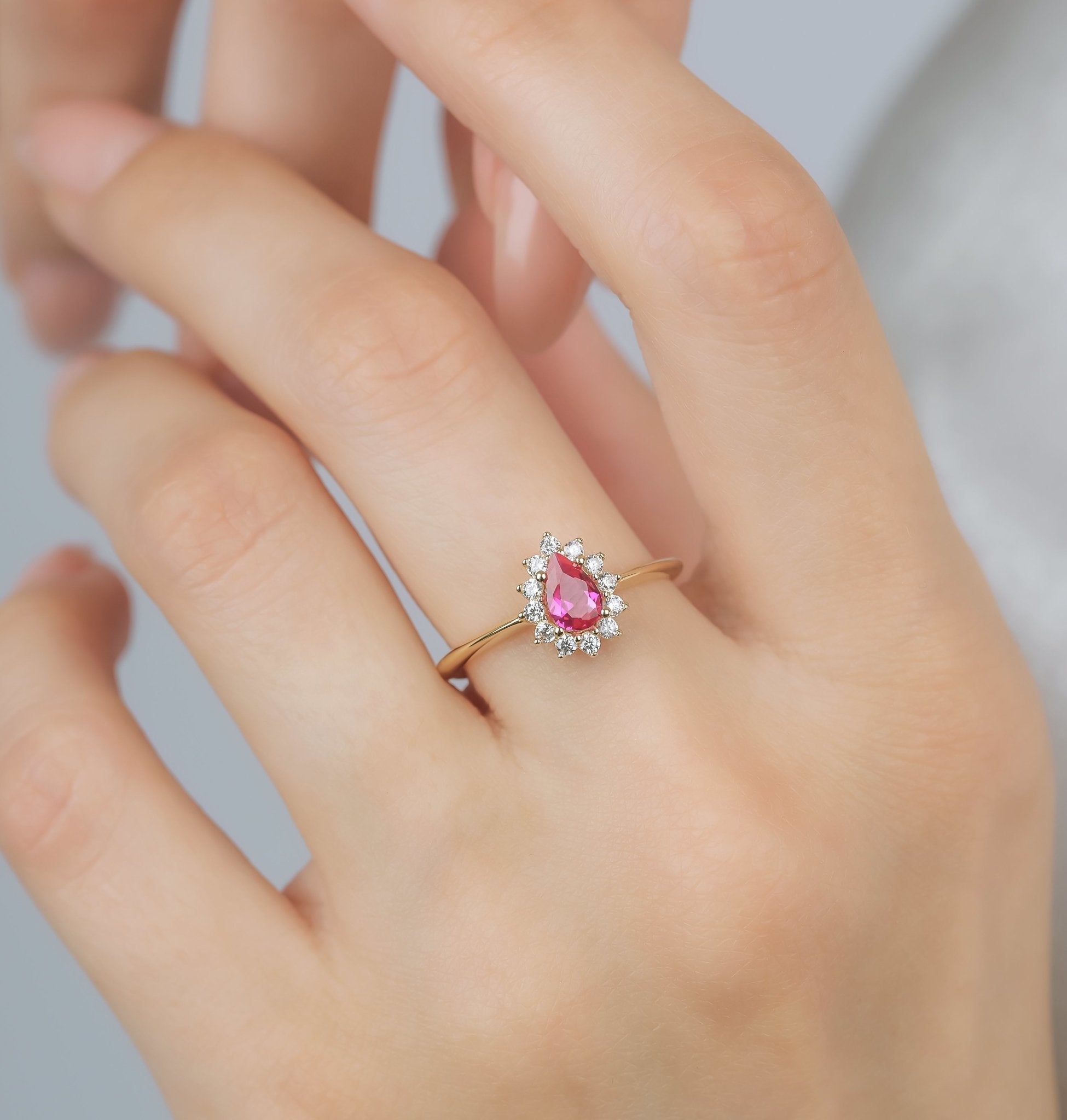 14K yellow gold pear shape ruby ring on model's hand with CZ accents, elegant womens wedding ring display.