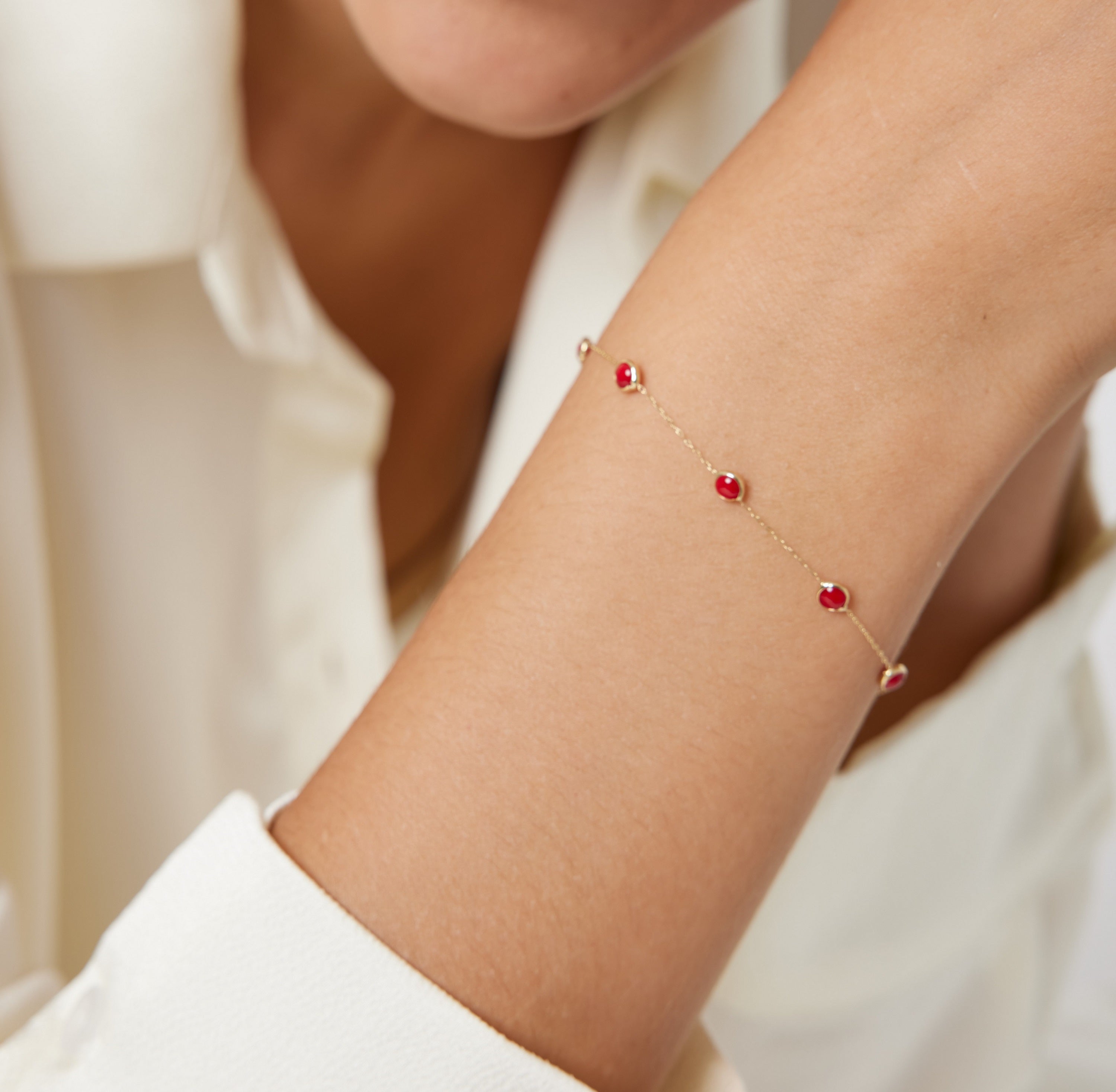 14K yellow gold beaded bracelet with red stones, elegantly worn on a wrist, showcasing minimalist style.