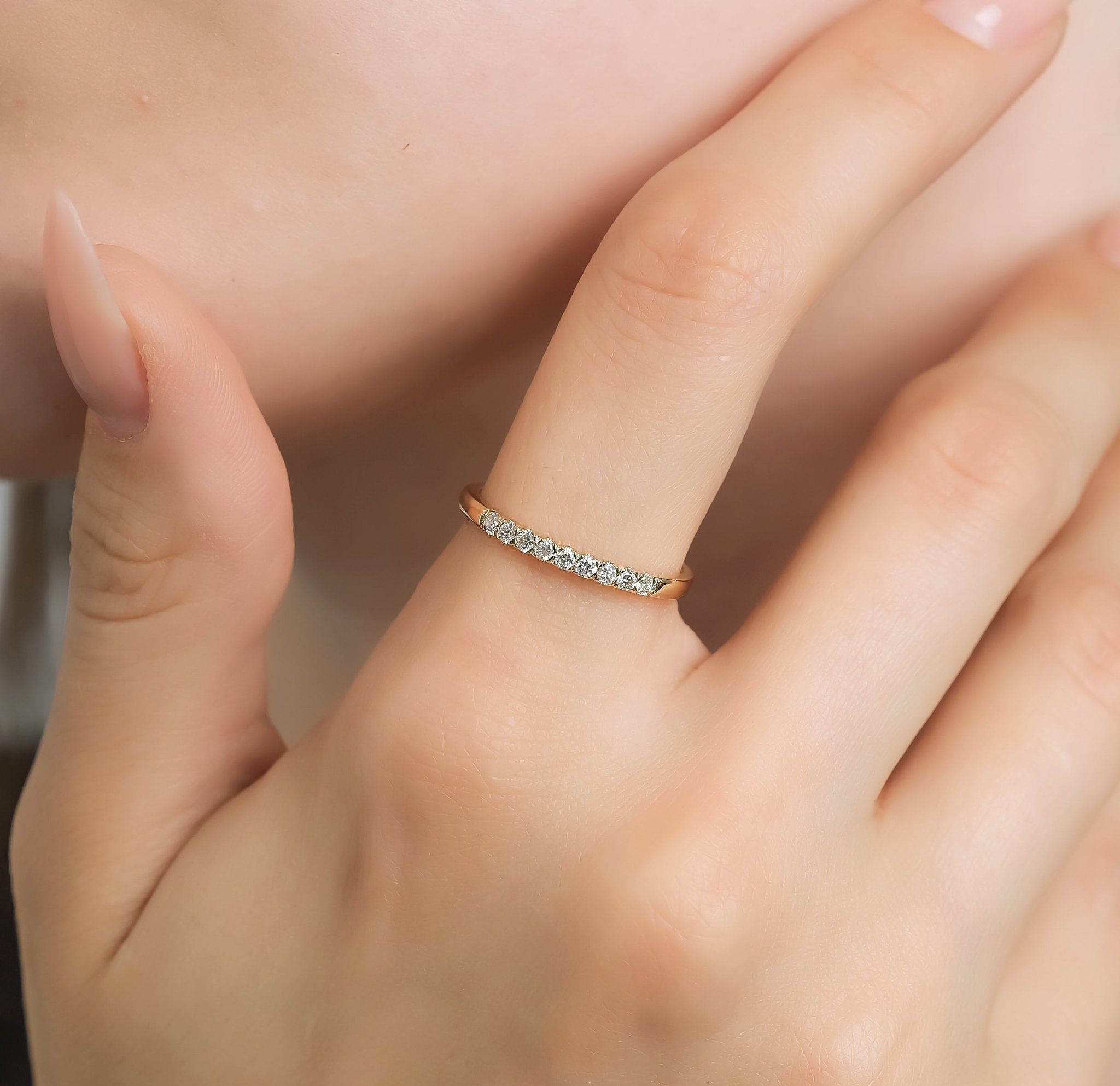 14K yellow gold diamond wedding band with 9 round diamonds, showcasing shiny finish and elegant design on model's hand.