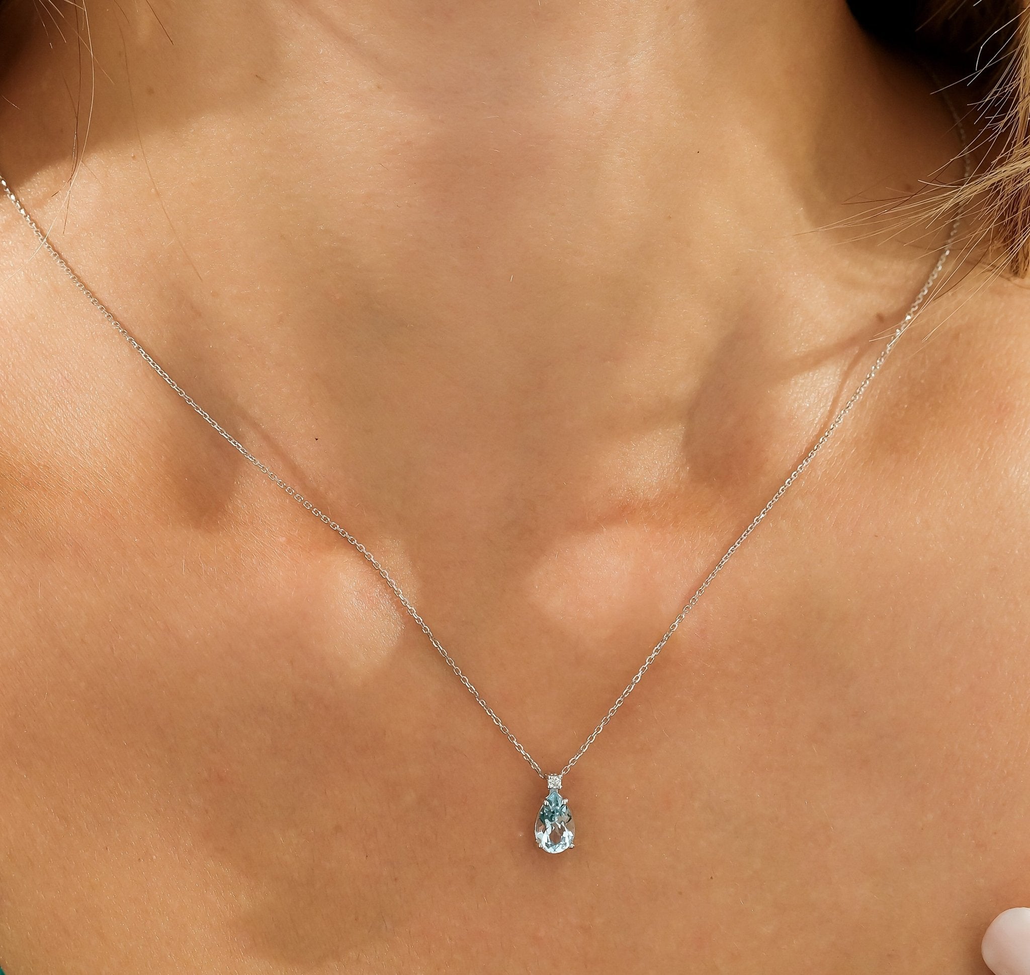 14K white gold pear shape blue topaz and diamond solitaire necklace worn on a model's neck.