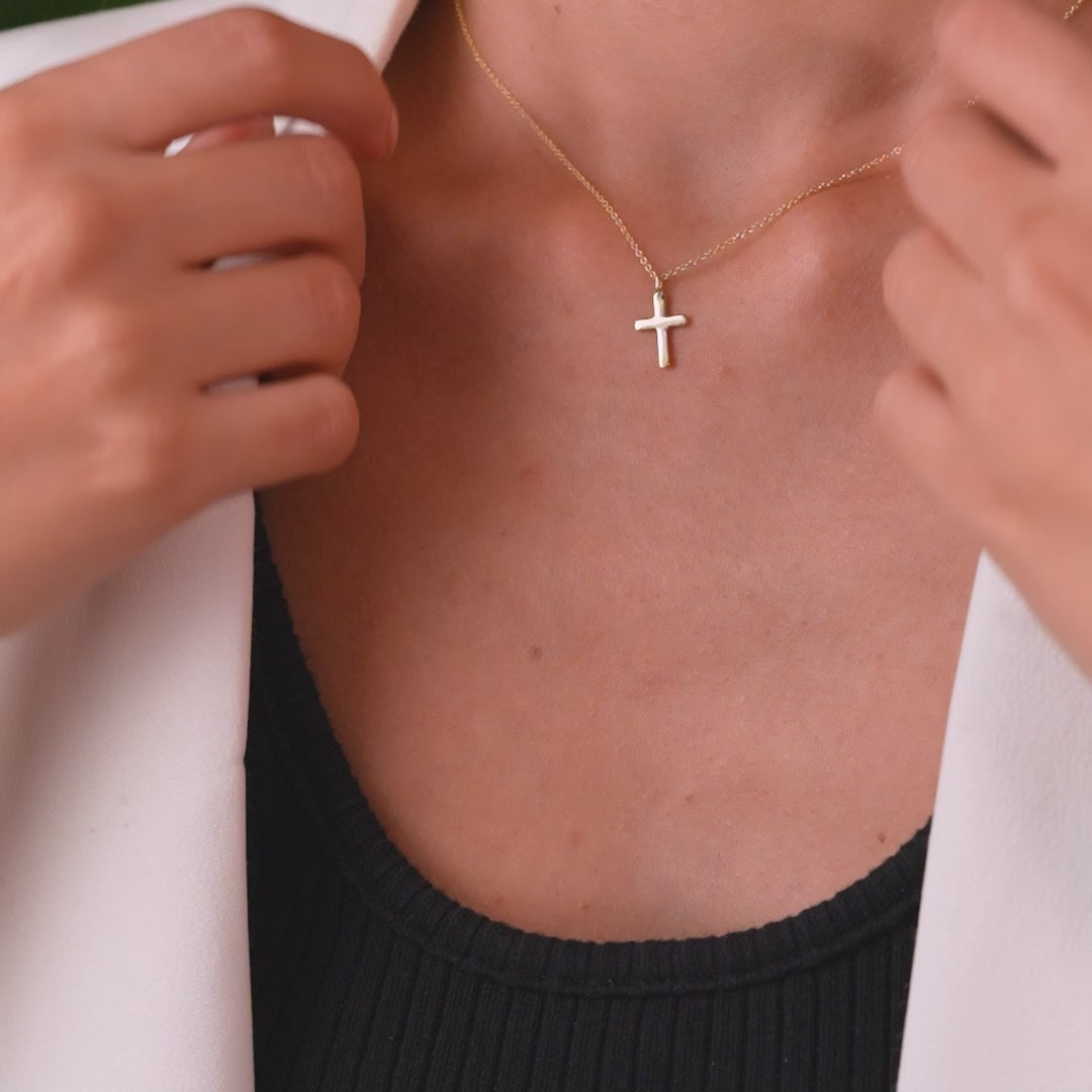 Model wearing a 14K solid yellow gold dainty cross necklace against a black shirt, showcasing minimalist jewelry style.