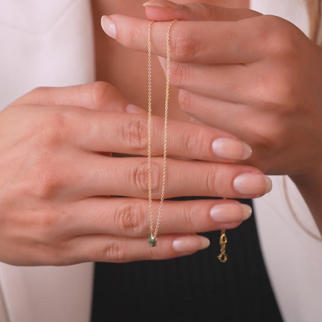 Woman holding a 14K yellow gold 6mm bezel set emerald solitaire necklace, showcasing its delicate design.
