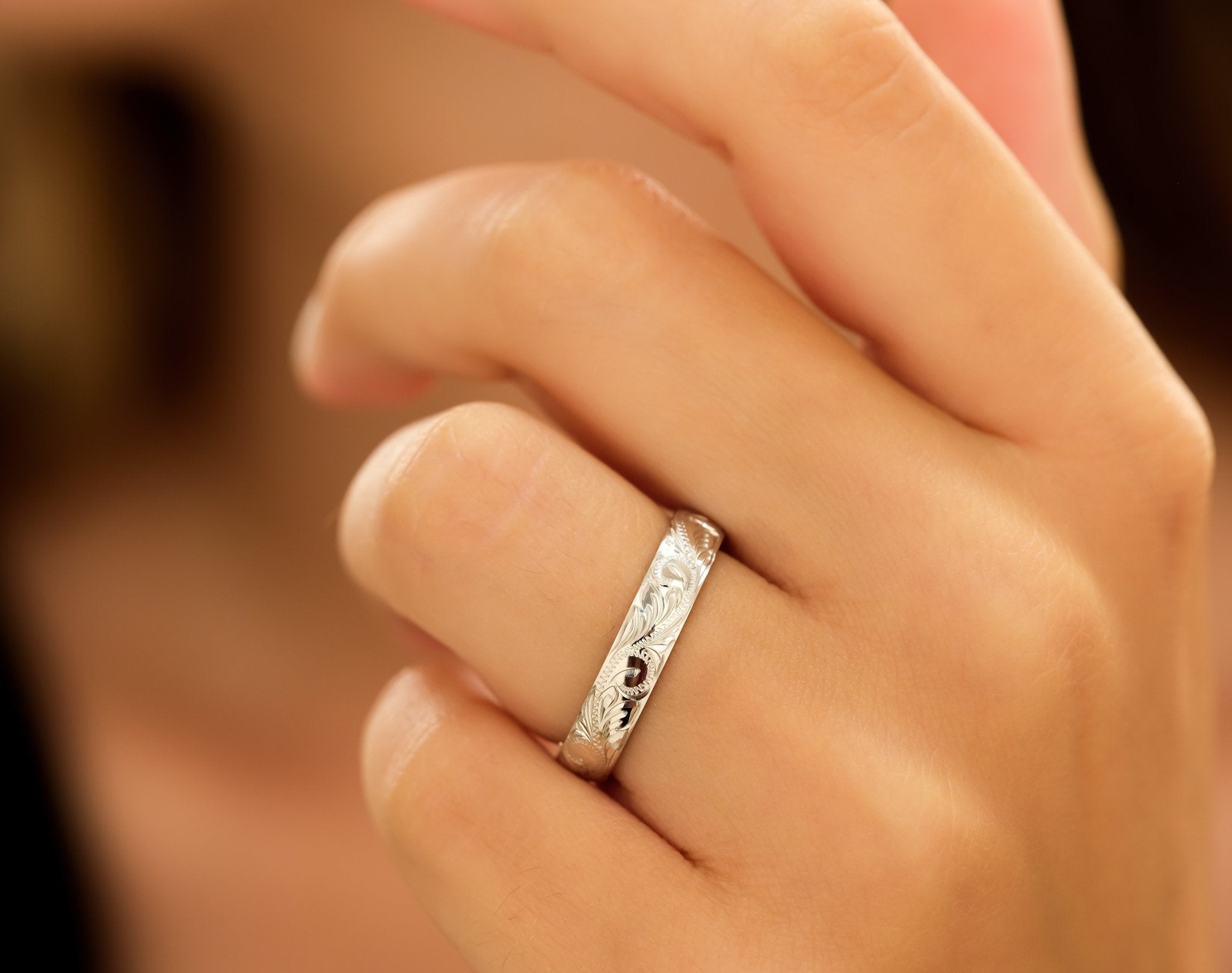 Hand showcasing a 4mm white gold wedding band with hand-engraved leaf motifs and shiny finish.