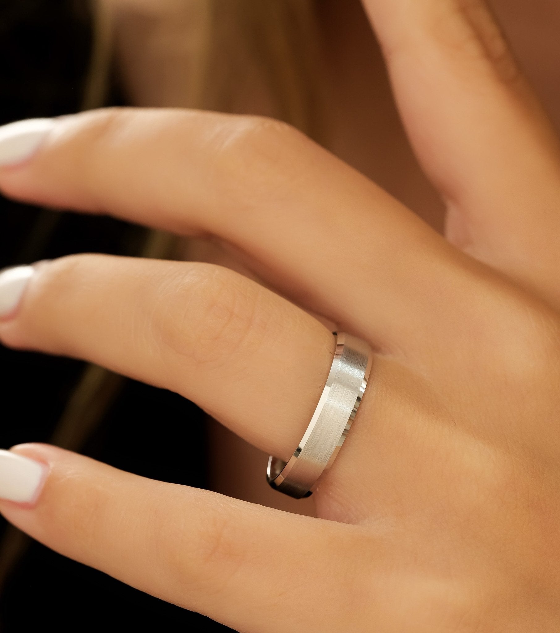 Close-up of a man's hand wearing a 5mm 14K white gold beveled edge wedding band with a satin finish.