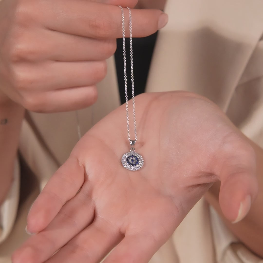 Dainty 14K solid gold evil eye pendant necklace displayed in hand, featuring a round design with CZ stones.