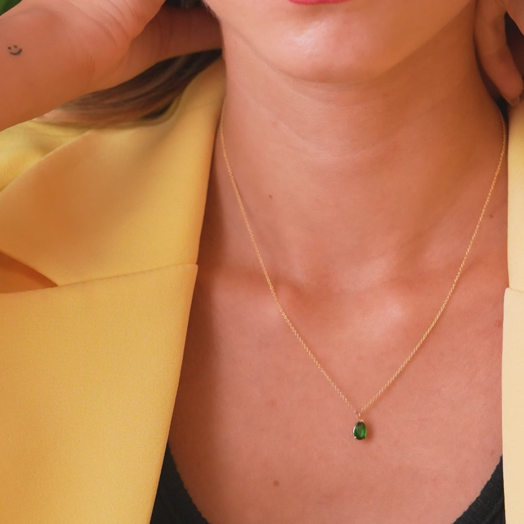 14K yellow gold pear shape emerald solitaire necklace worn by a woman, highlighting its dainty and minimalist design.