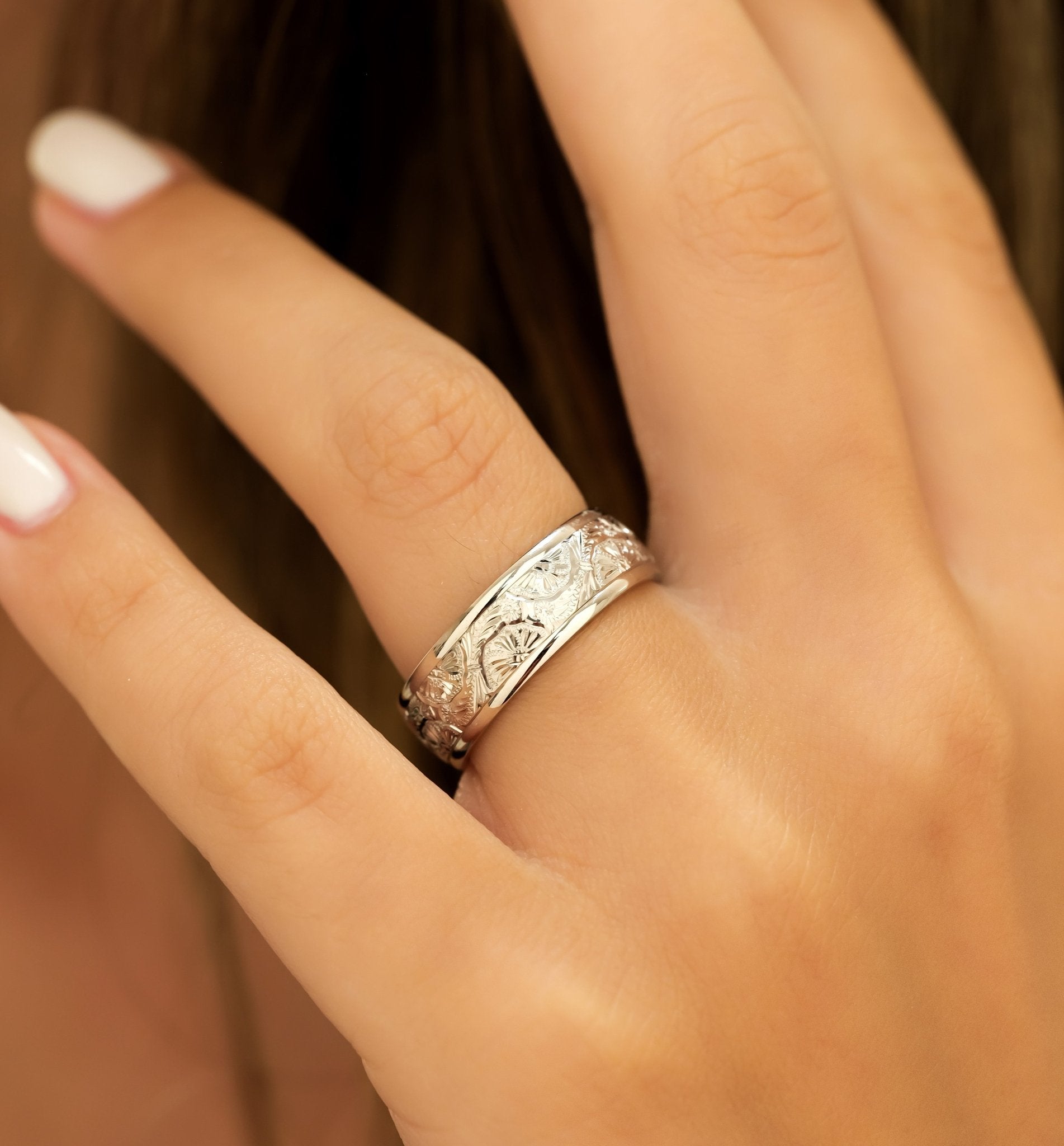Hand engraved 7mm white gold wedding band featuring a leaf motif, showcased on a finger with a shiny finish.