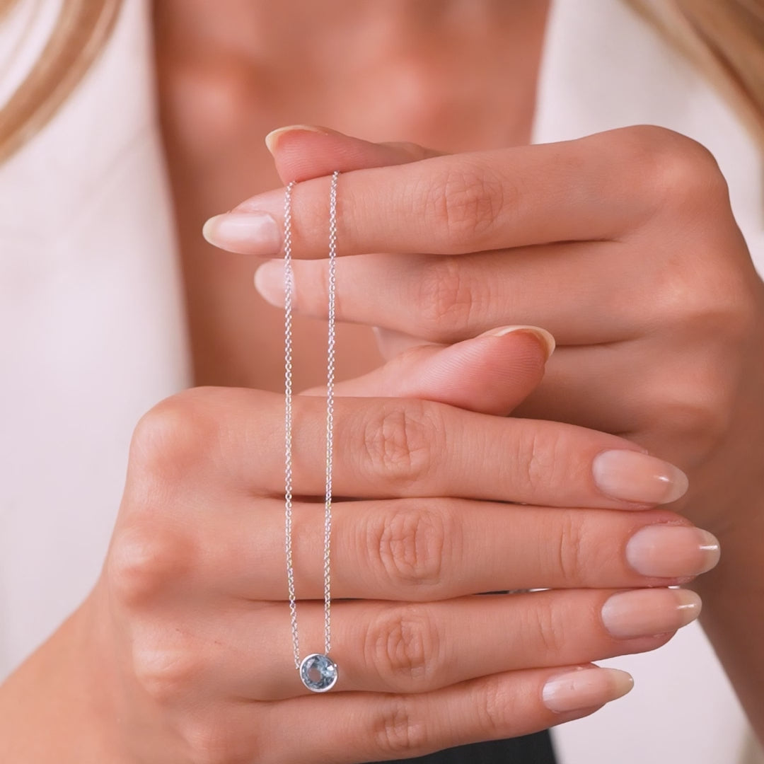 Woman holding a 14K yellow gold bezel set aquamarine solitaire necklace, showcasing its elegance and simplicity.