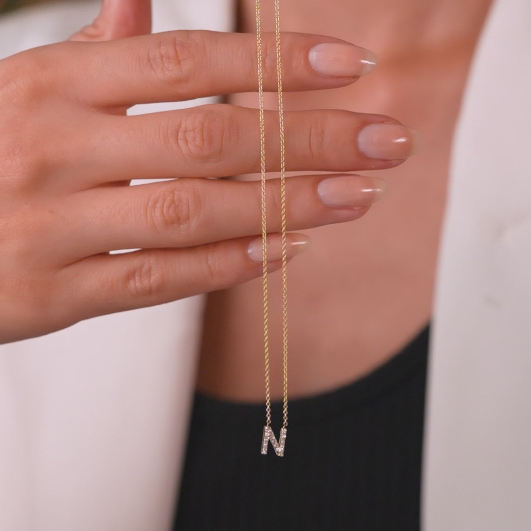 14K yellow gold initial necklace with diamond letter N, held in hand, dainty design and sparkle.