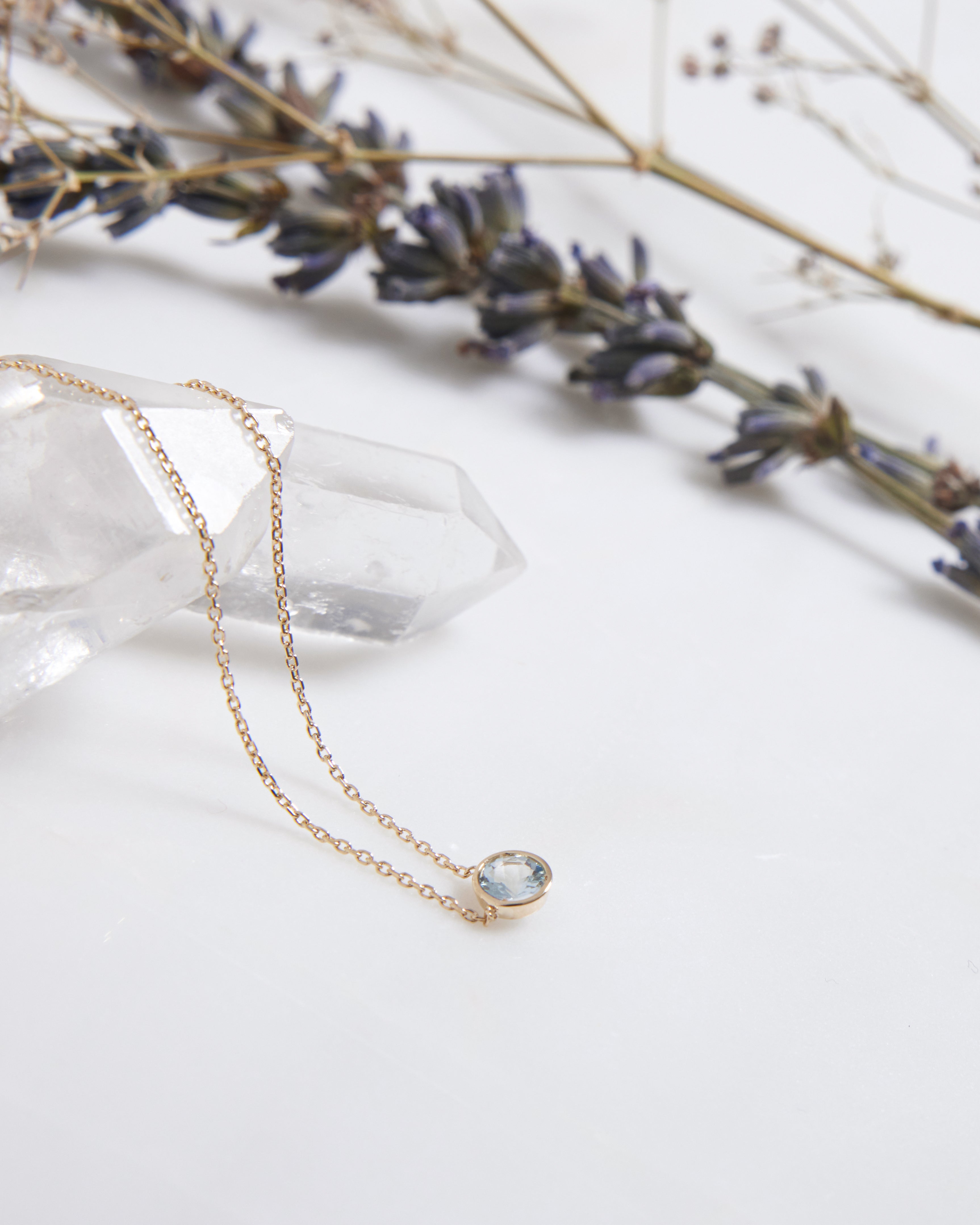 14K yellow gold 6mm bezel set solitaire aquamarine necklace on a crystal with lavender accents, minimalist design.