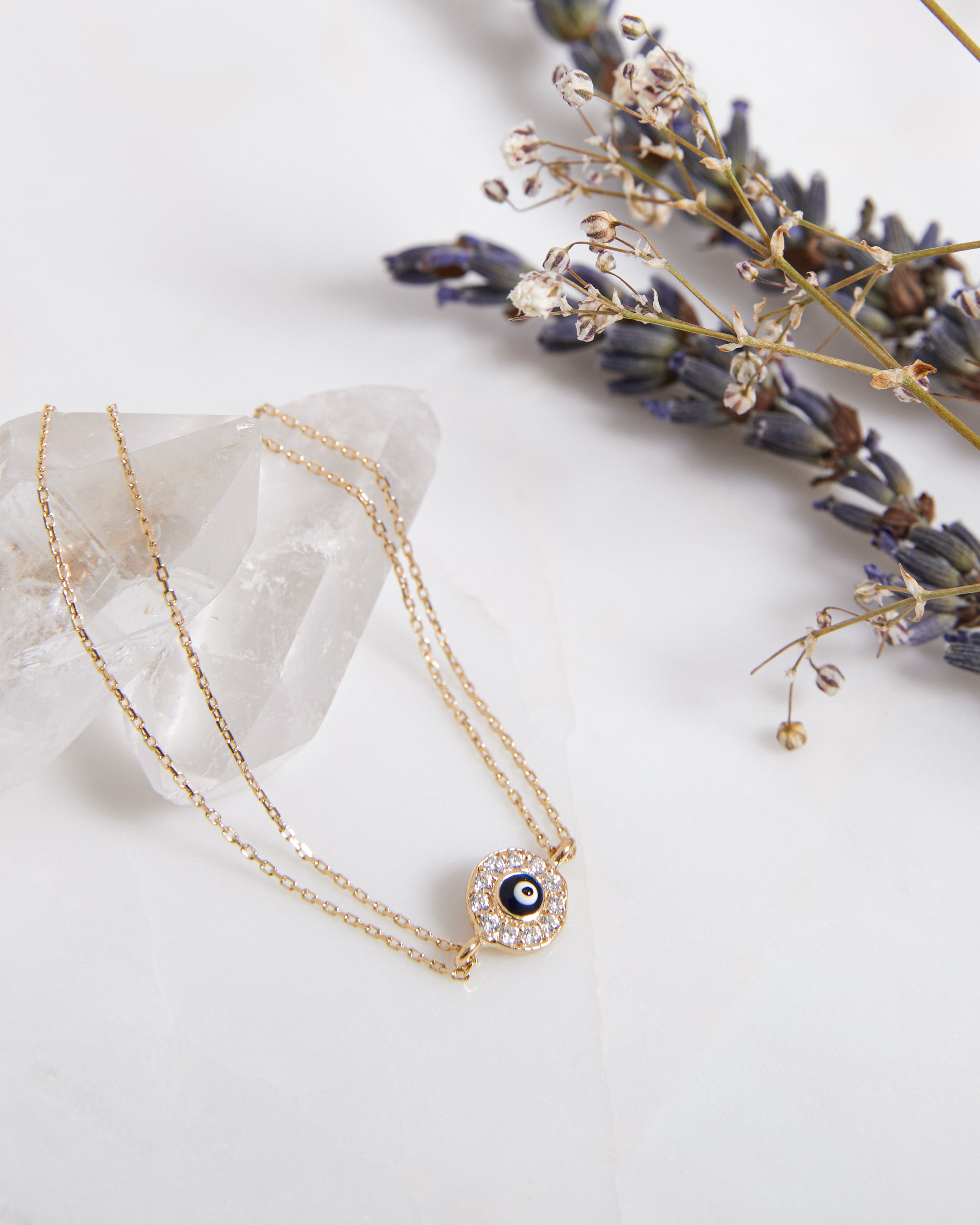 14K solid yellow gold round evil eye bracelet with CZ on a marble surface with dried flowers.