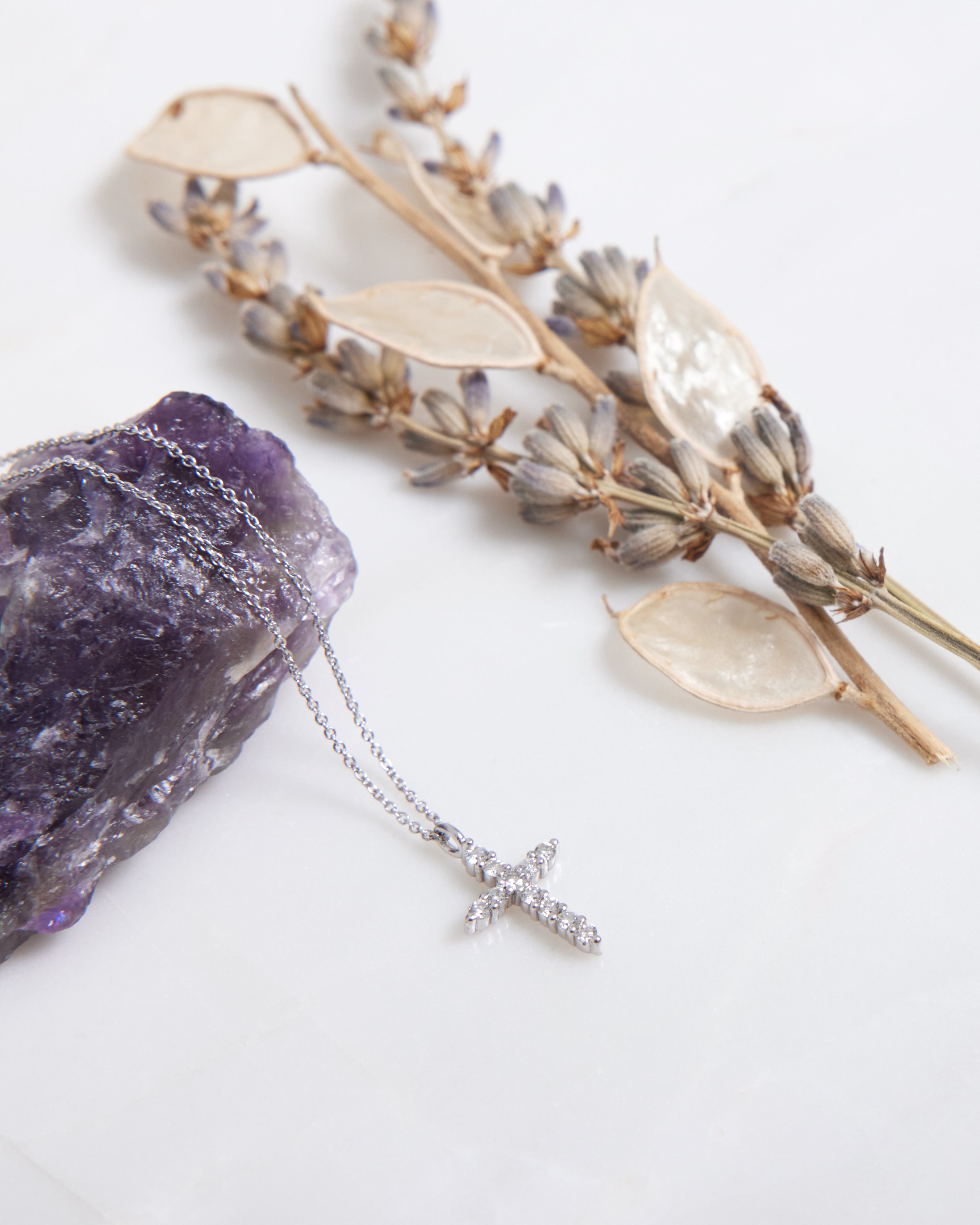 14K solid white gold diamond cross necklace on a marble surface with lavender and purple crystal accents.