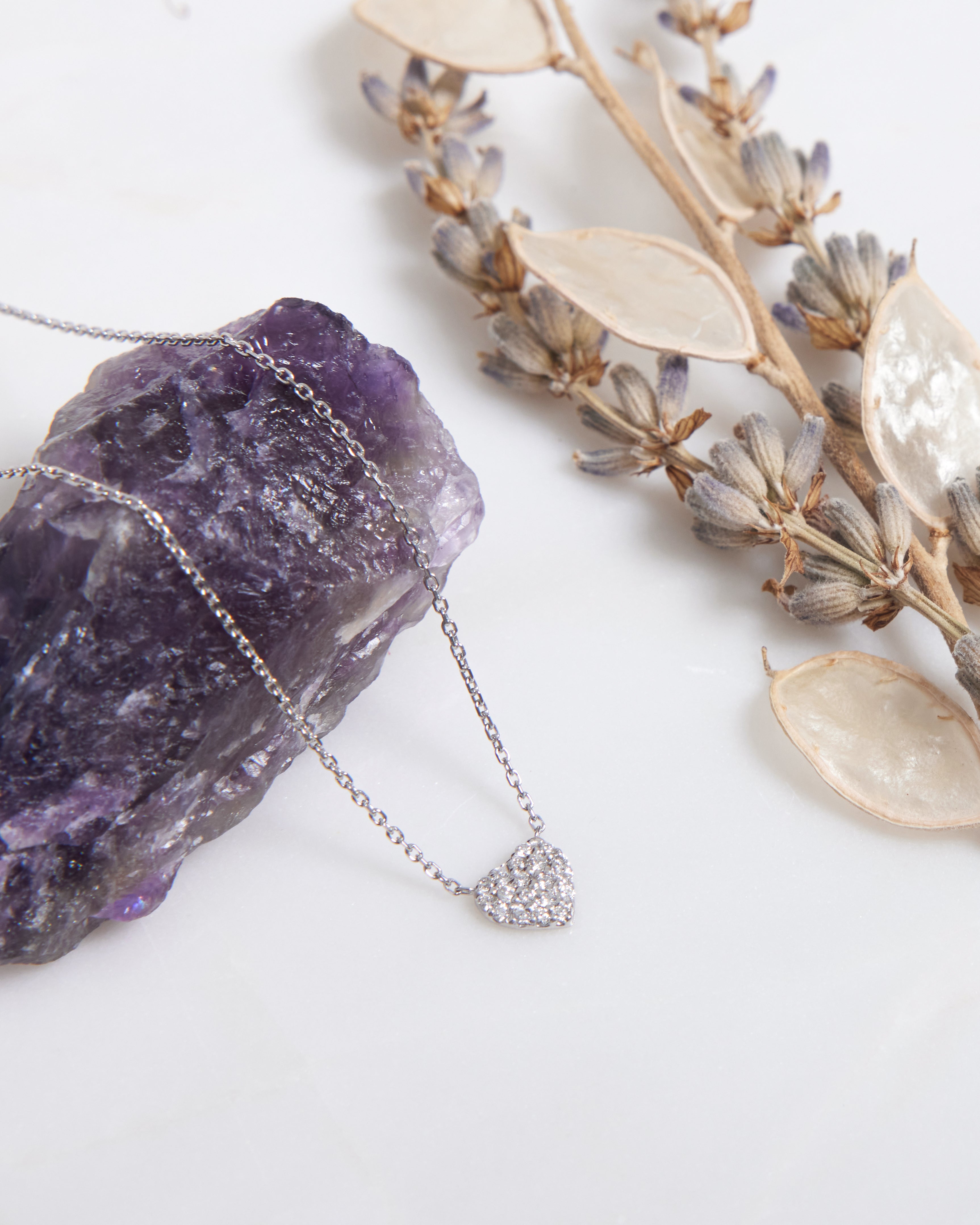14K solid white gold minimalist diamond heart necklace resting on a purple crystal, showcasing its dainty design.