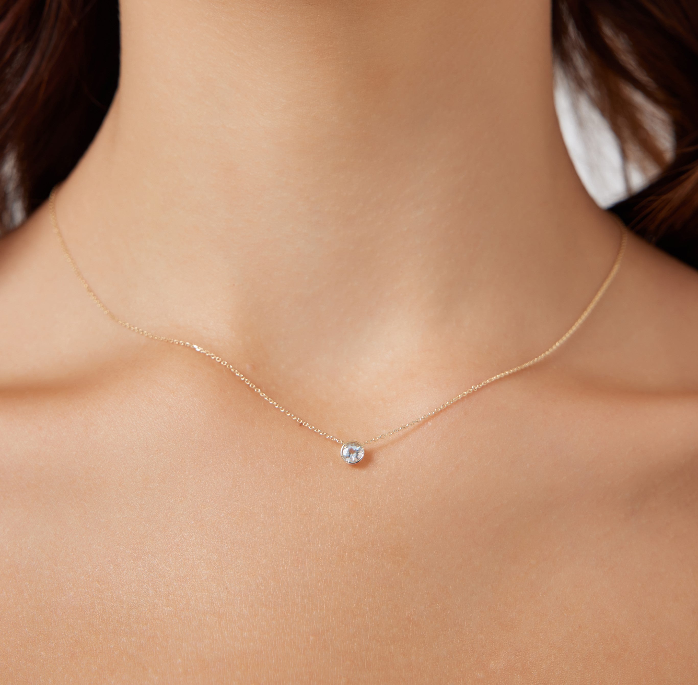 Dainty 14K yellow gold necklace featuring a 4mm bezel set aquamarine solitaire pendant against a neutral background.