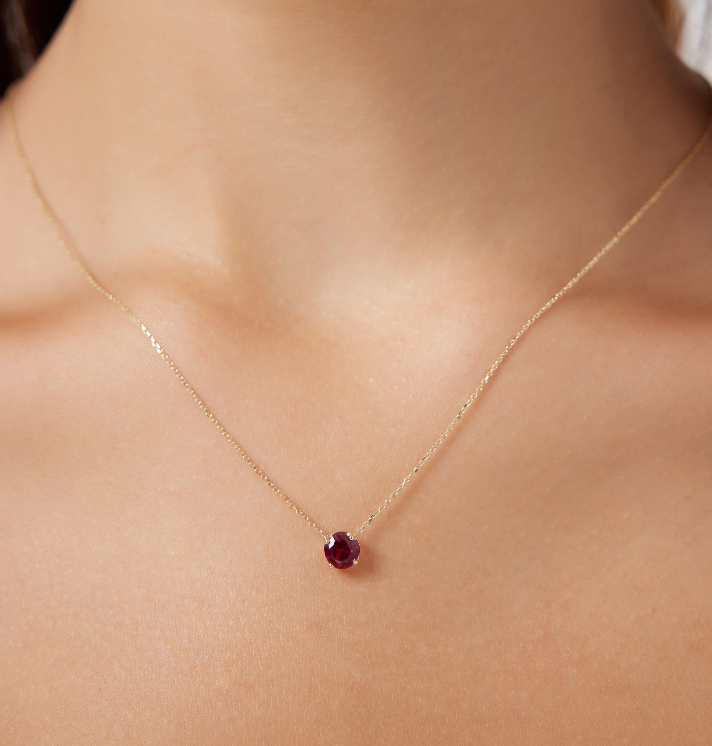 Dainty 14K yellow gold 6mm prong setting ruby solitaire necklace worn on a model's neck.