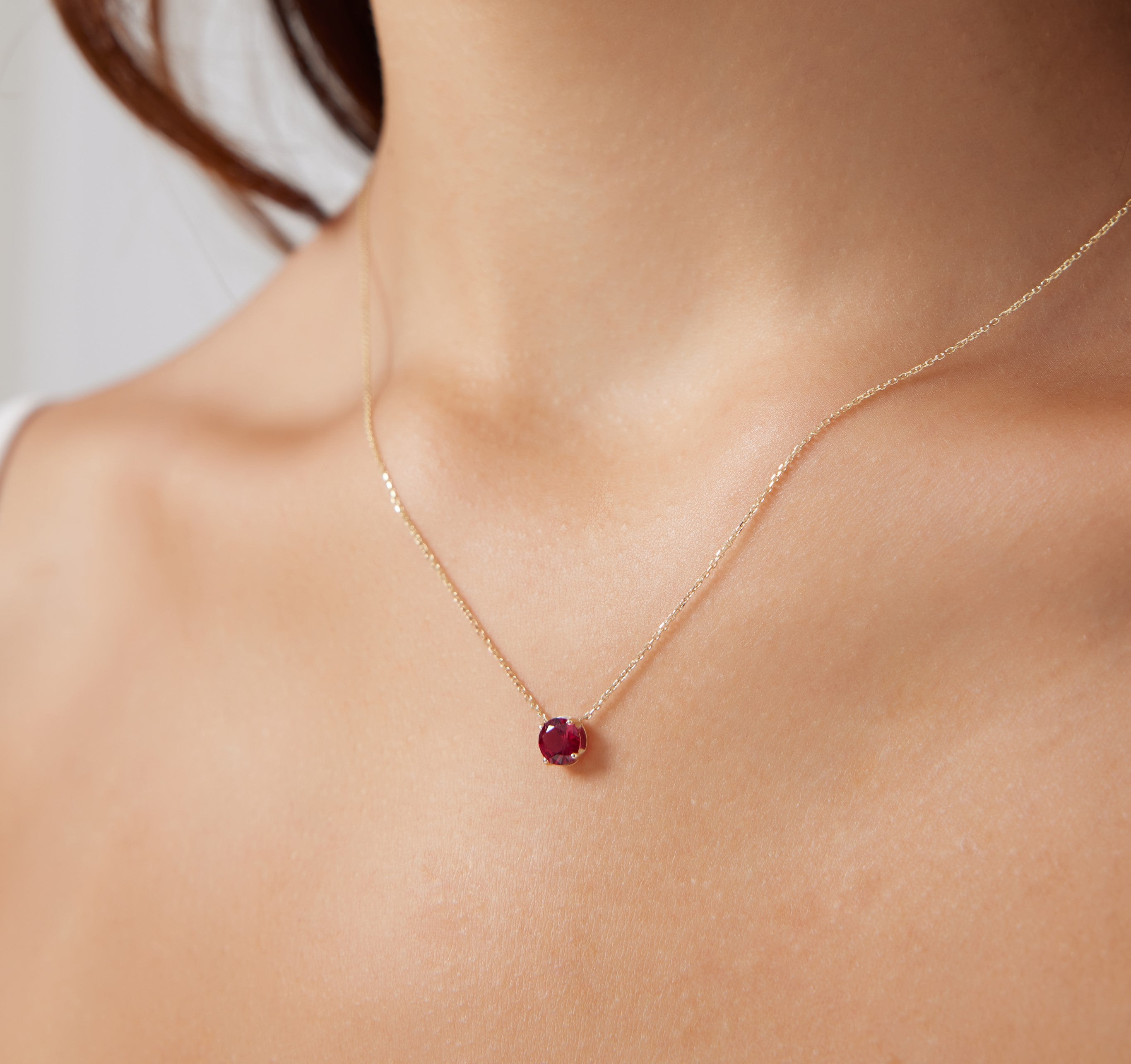 14K yellow gold 6mm prong setting ruby solitaire necklace worn on a woman's neck, showcasing July's birthstone.