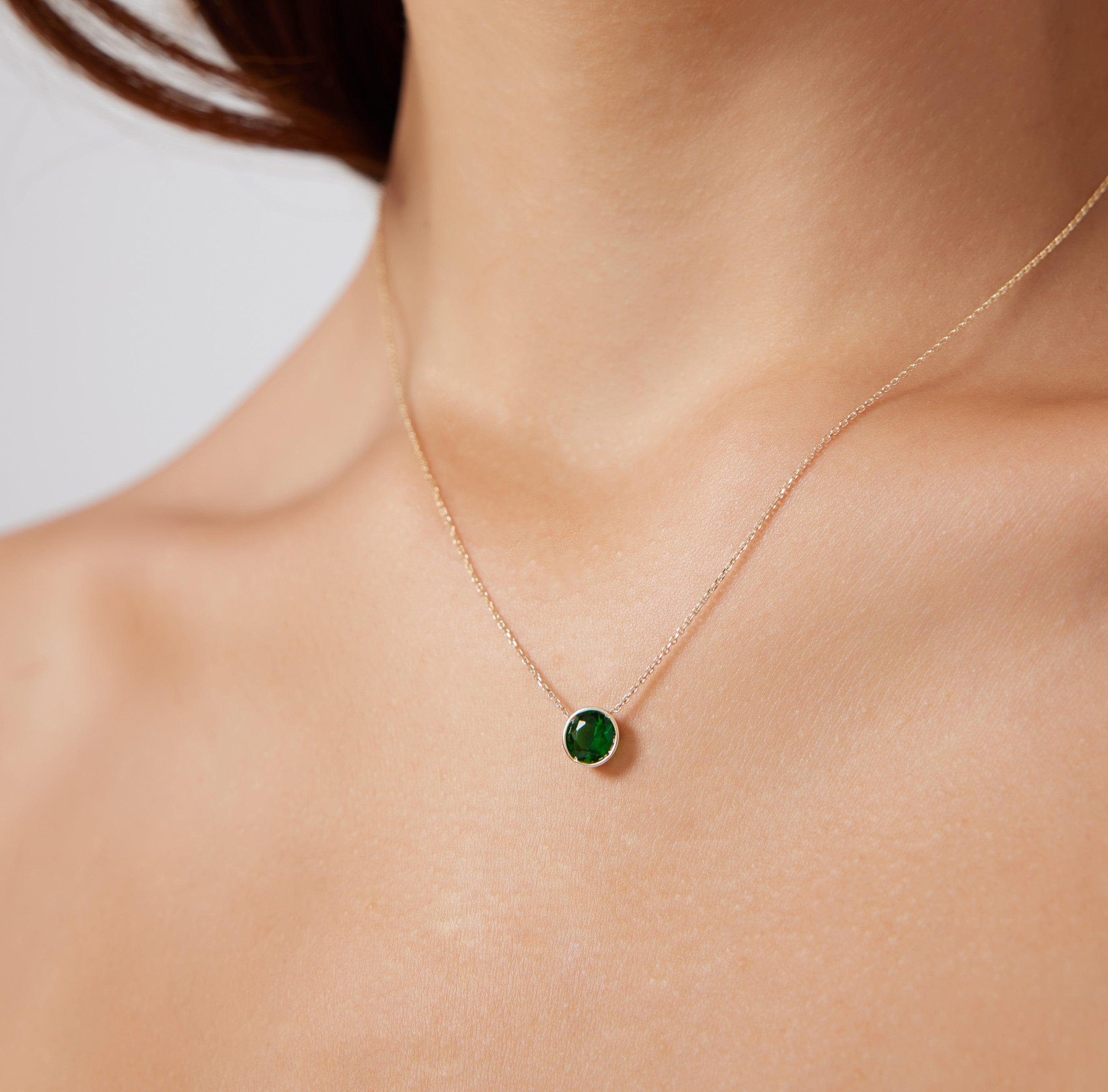 14K yellow gold 6mm bezel set emerald solitaire necklace worn on a model's neck, showcasing a dainty and elegant design.
