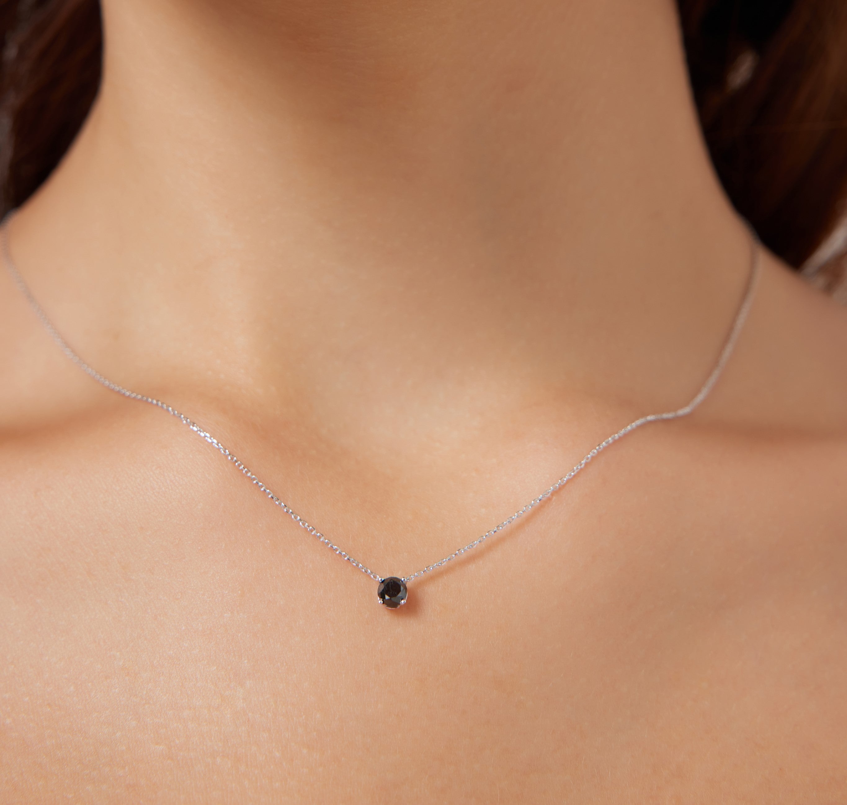 14K white gold minimalist black diamond solitaire necklace worn by a woman, highlighting its elegant simplicity.