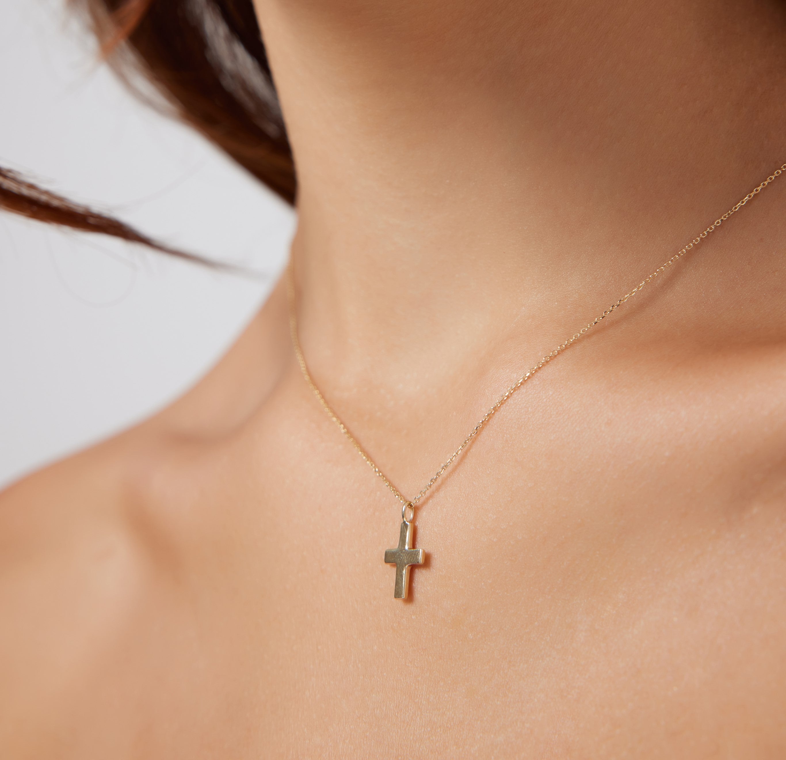 Close-up of a woman wearing a 14K solid yellow gold dainty cross necklace on her neck.