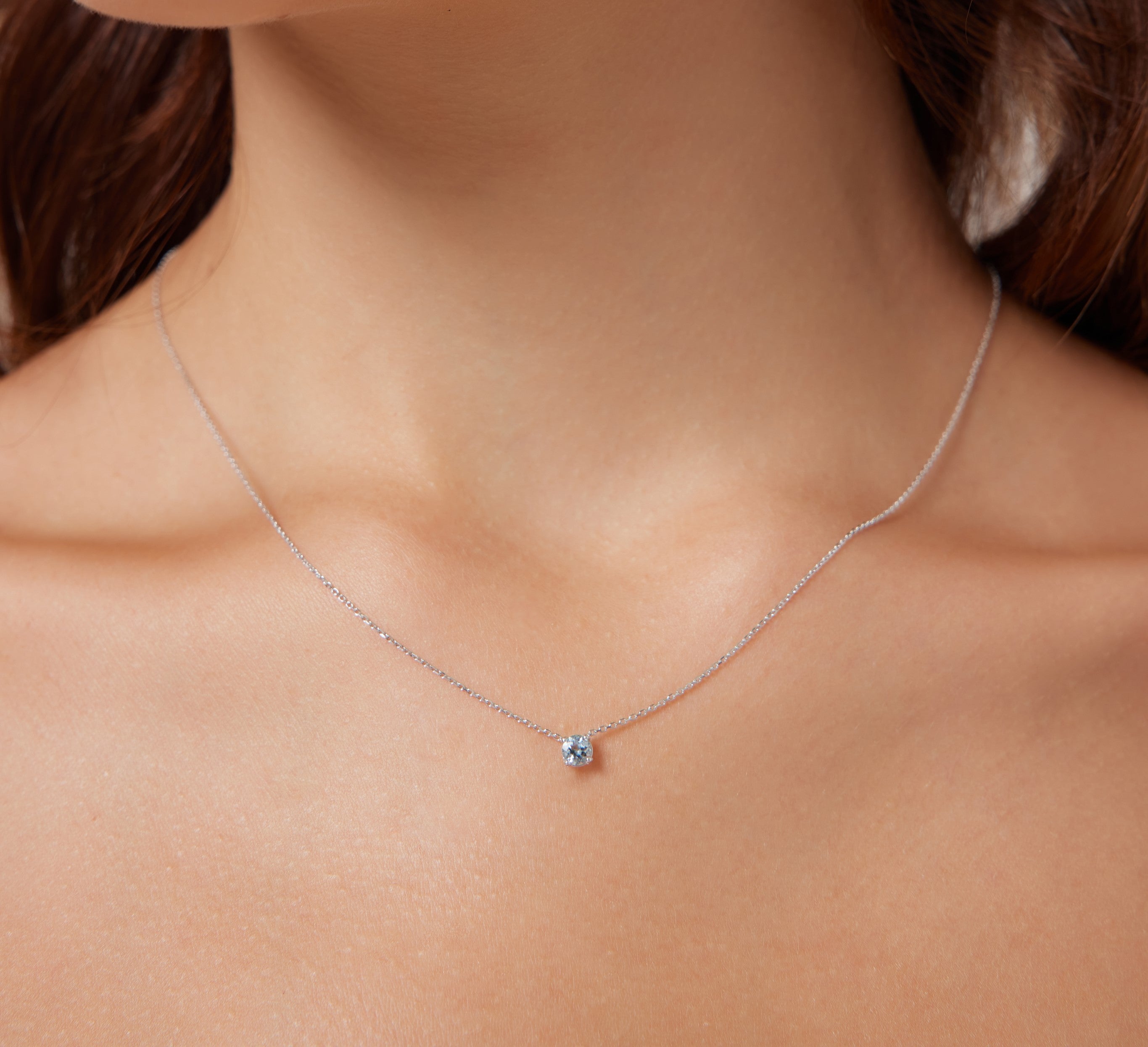 Delicate 14K white gold prong setting solitaire aquamarine necklace worn on a woman's neck, showcasing its minimalist design.