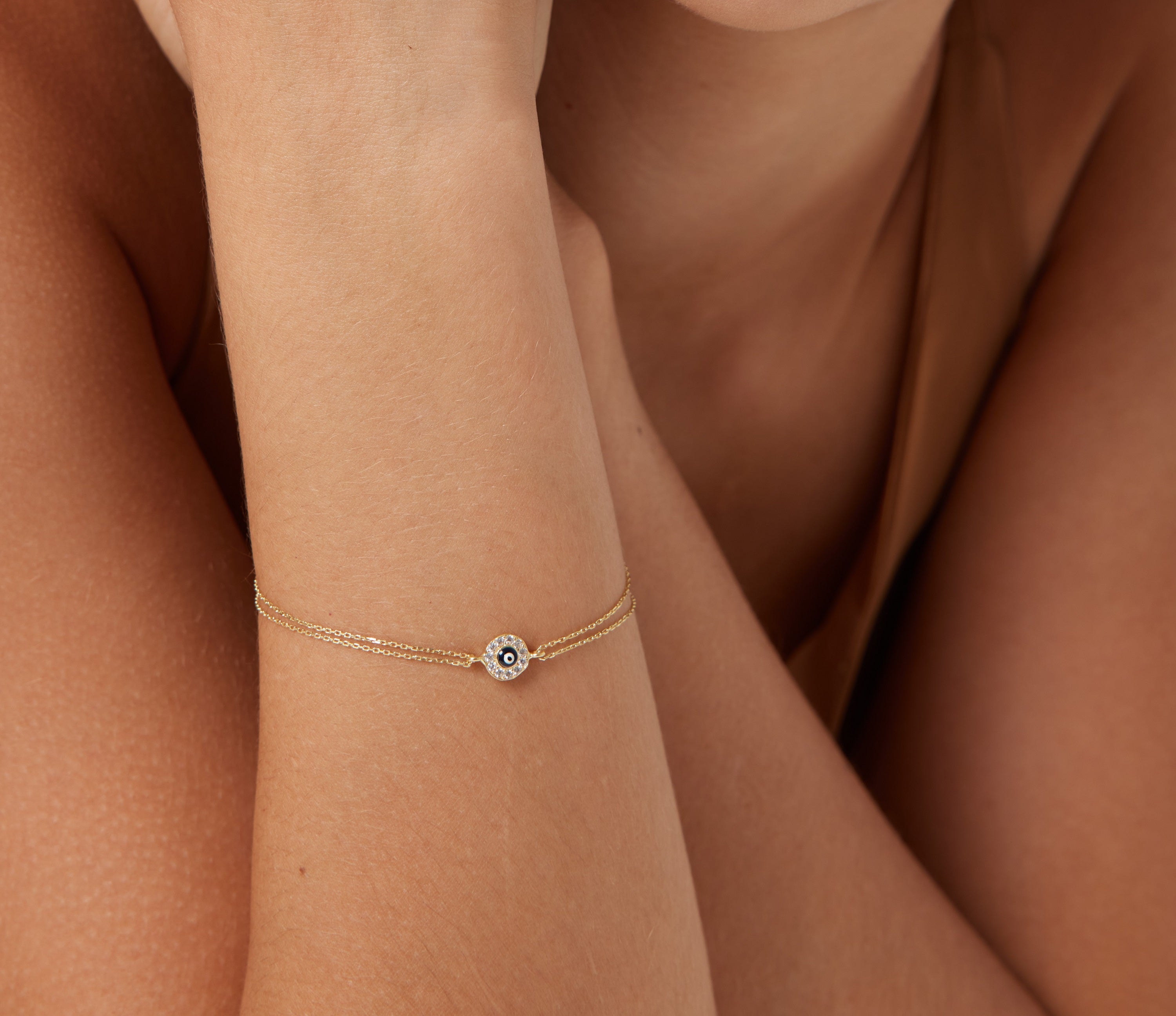14K solid yellow gold round evil eye bracelet worn on a model's wrist, featuring a delicate minimalist design.
