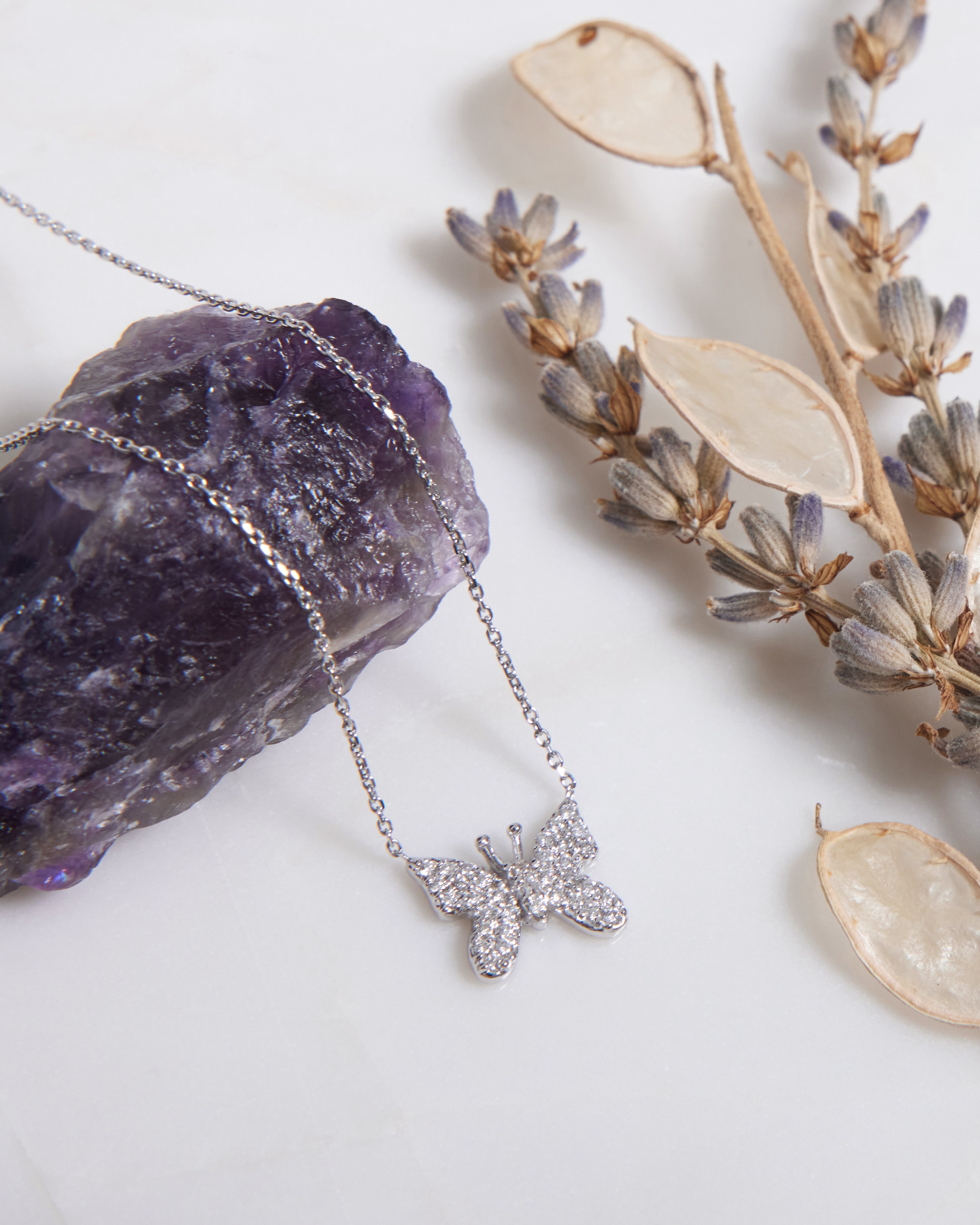 14K solid white gold butterfly necklace with diamond accents on a purple stone background.