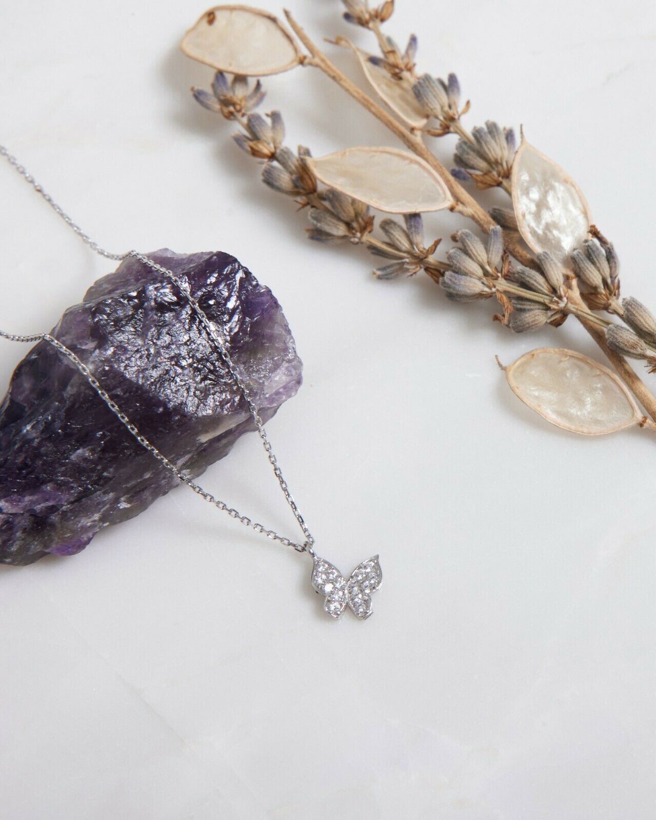14K solid white gold minimalist butterfly necklace displayed on amethyst stone with dried leaves background.