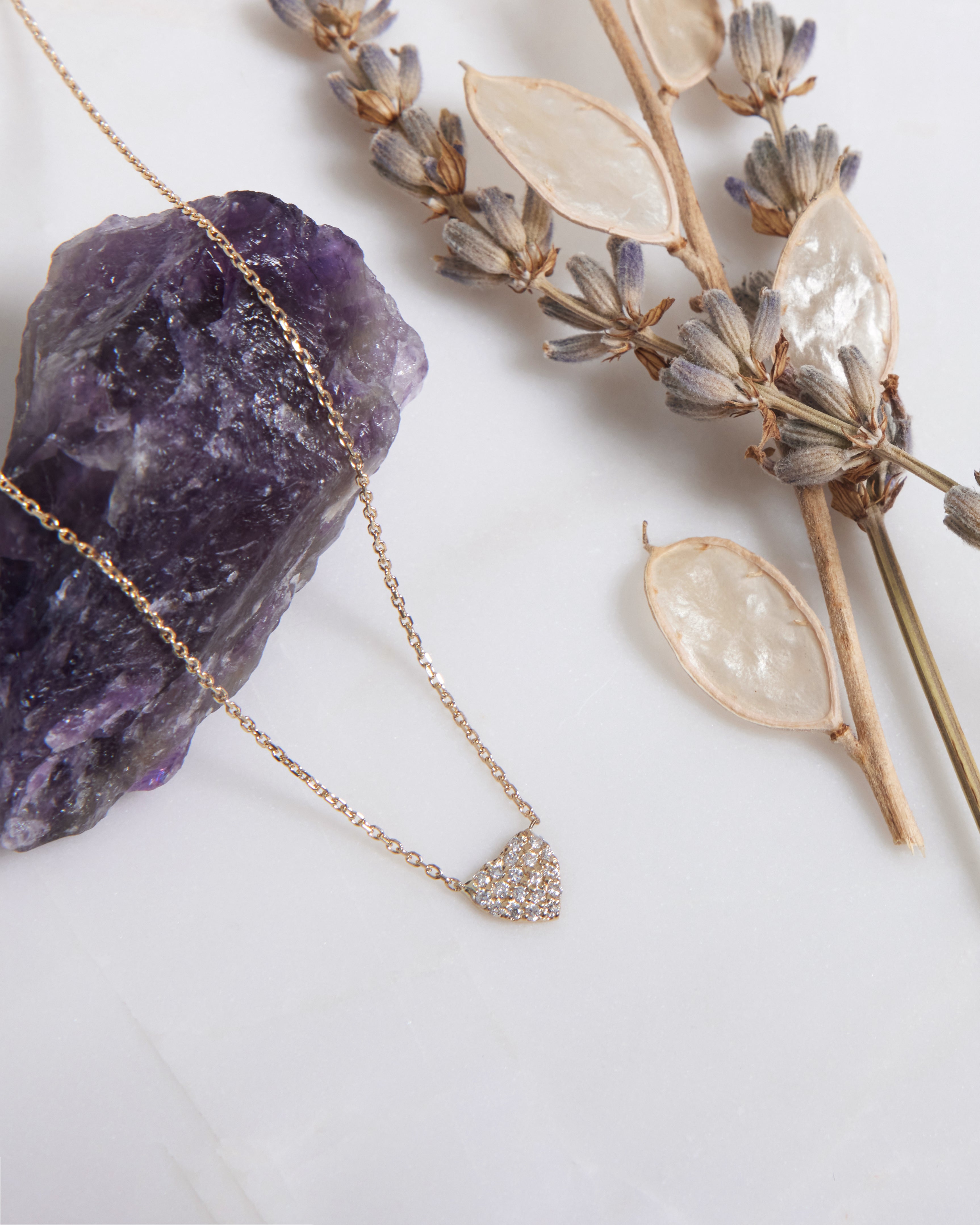 14K solid yellow gold minimalist diamond heart necklace displayed with amethyst and dried flowers.