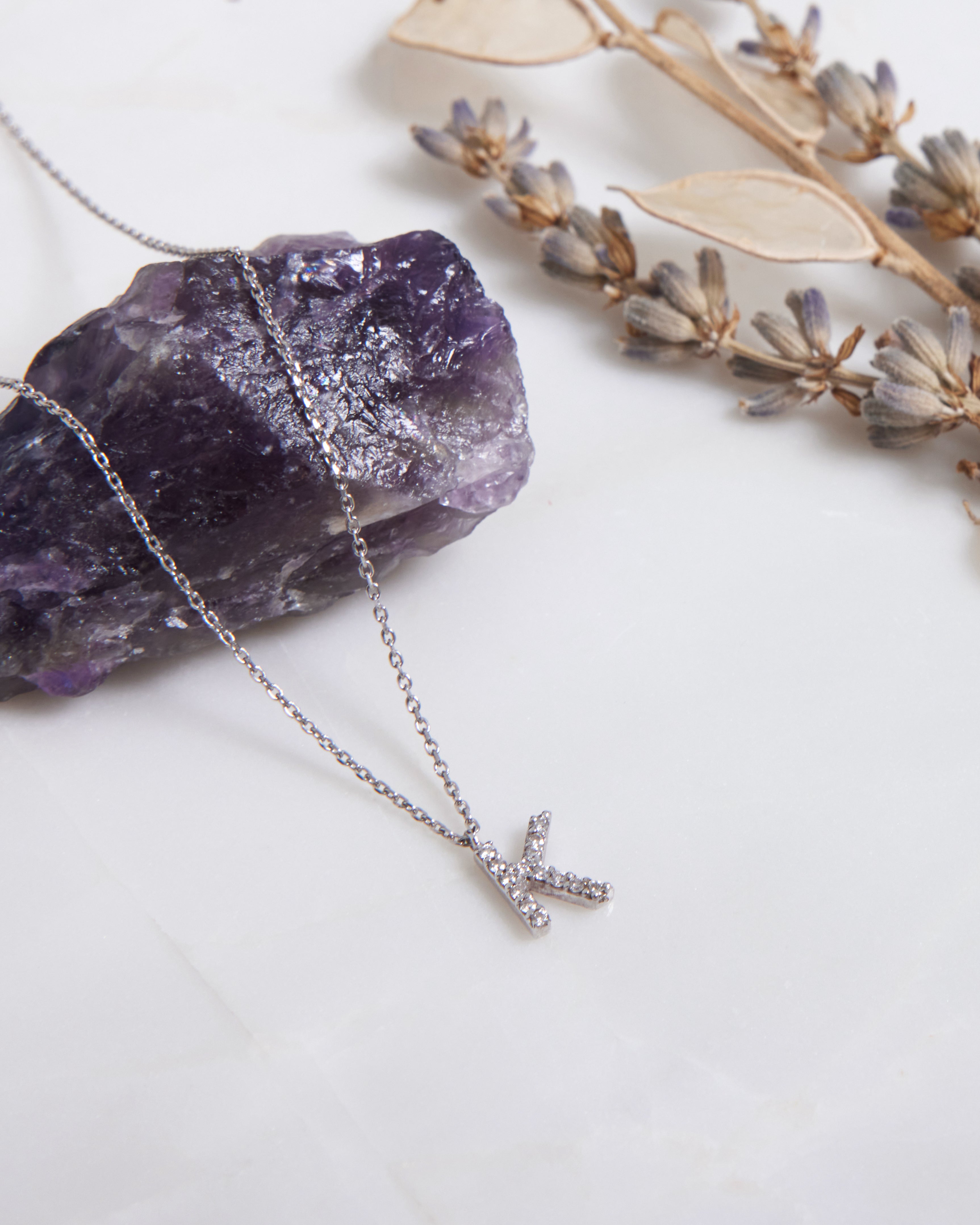 14K gold initial necklace with diamond letter K on a purple stone background.